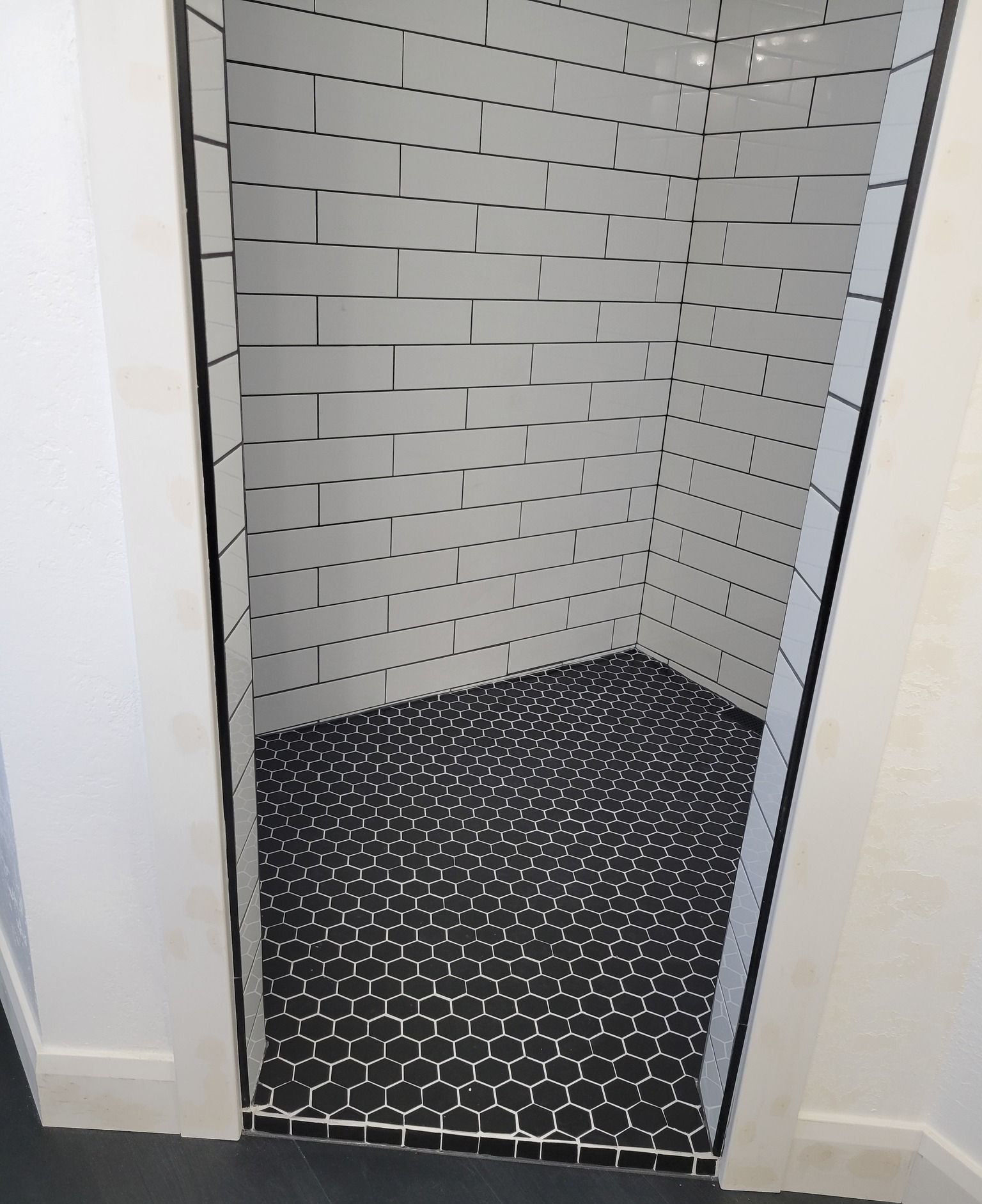 A shower stall with white subway tile walls and a black hexagonal tile floor.
