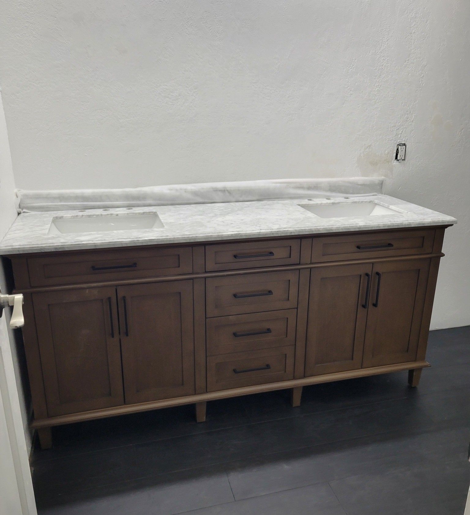 A double-sink bathroom vanity with a white marble top and wooden cabinets against a white wall.