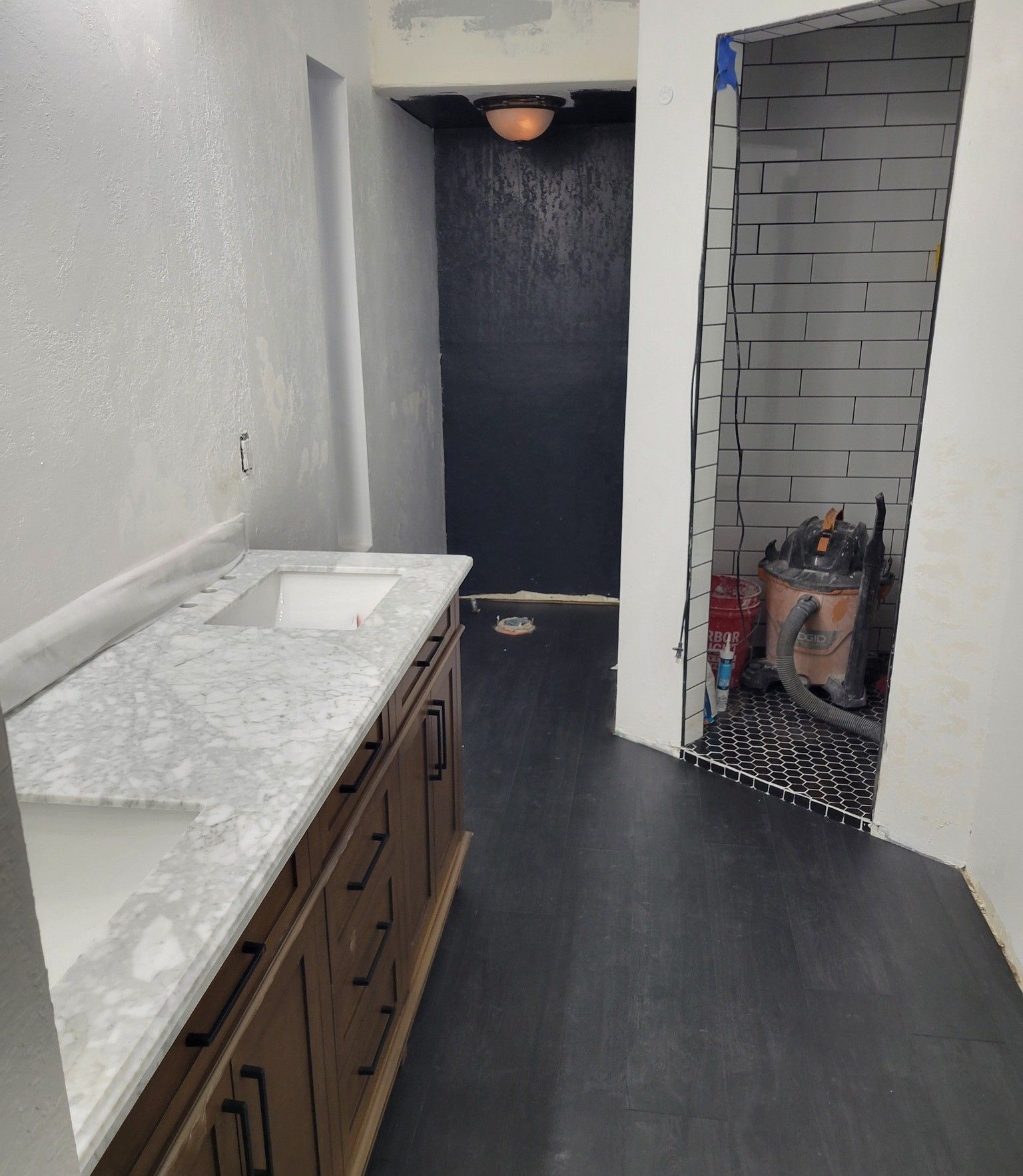A bathroom undergoing renovation with a new marble vanity, dark flooring, and an open, unfinished shower area.
