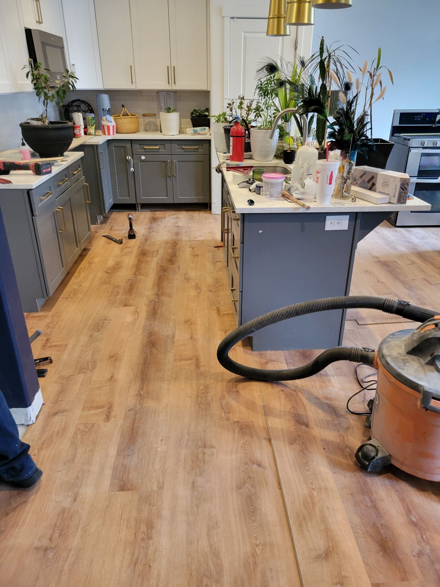 A kitchen under renovation with wood-look flooring, gray cabinets, a white island, and a shop vacuum on the floor.