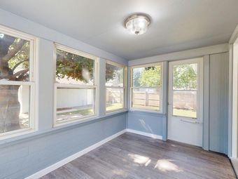 A sunroom with light blue walls, wood-look flooring, a ceiling light, large windows, and a glass-paneled door.