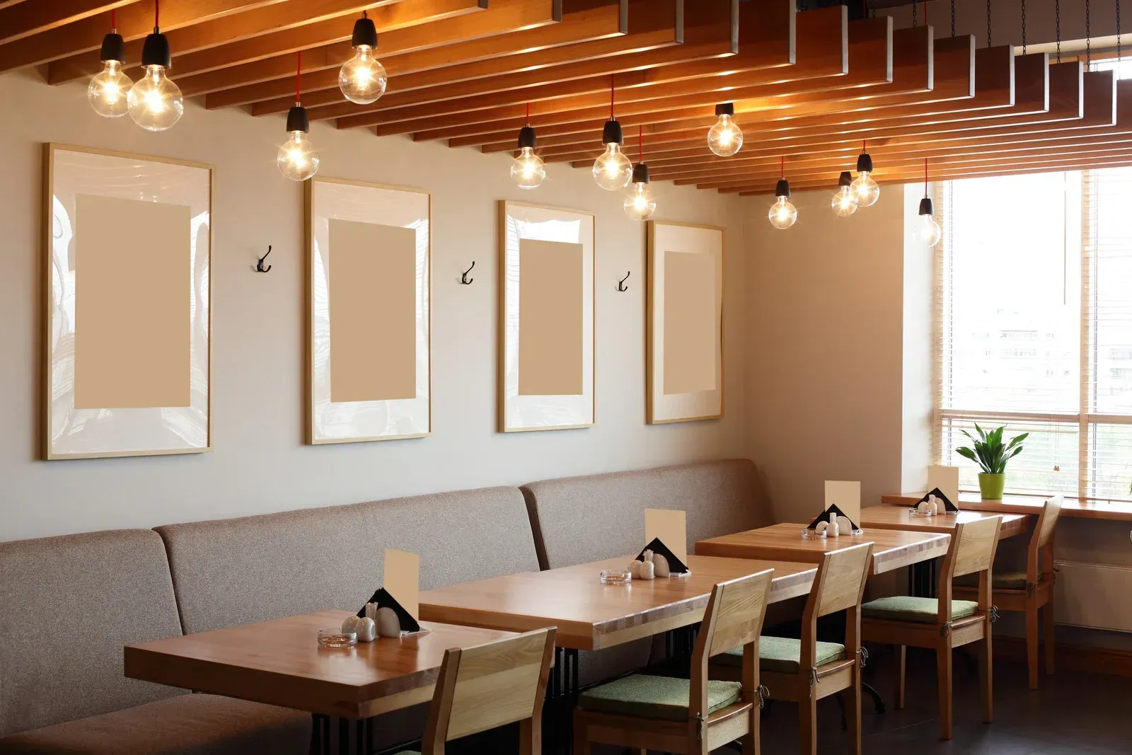 A bright, modern cafe interior with wooden slatted ceilings, pendant lights, framed wall art, and tables with chairs.