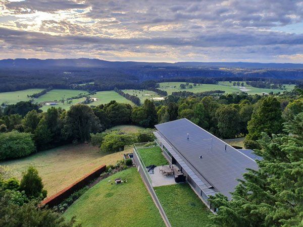Modern house with a green roof overlooks a lush valley at sunset.