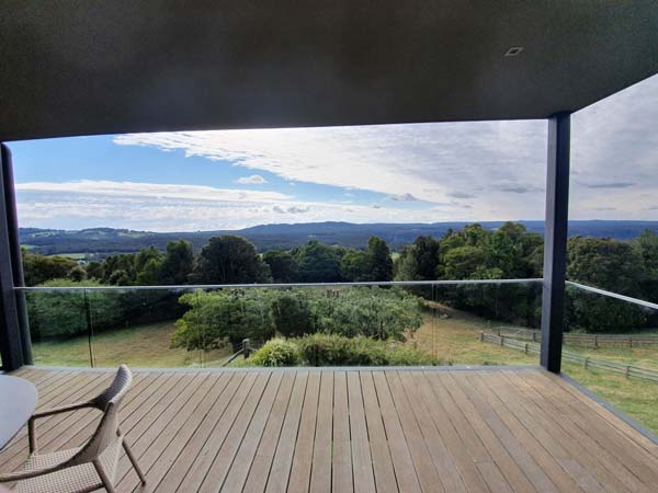 Wooden deck overlooking a green landscape and blue sky with clouds.