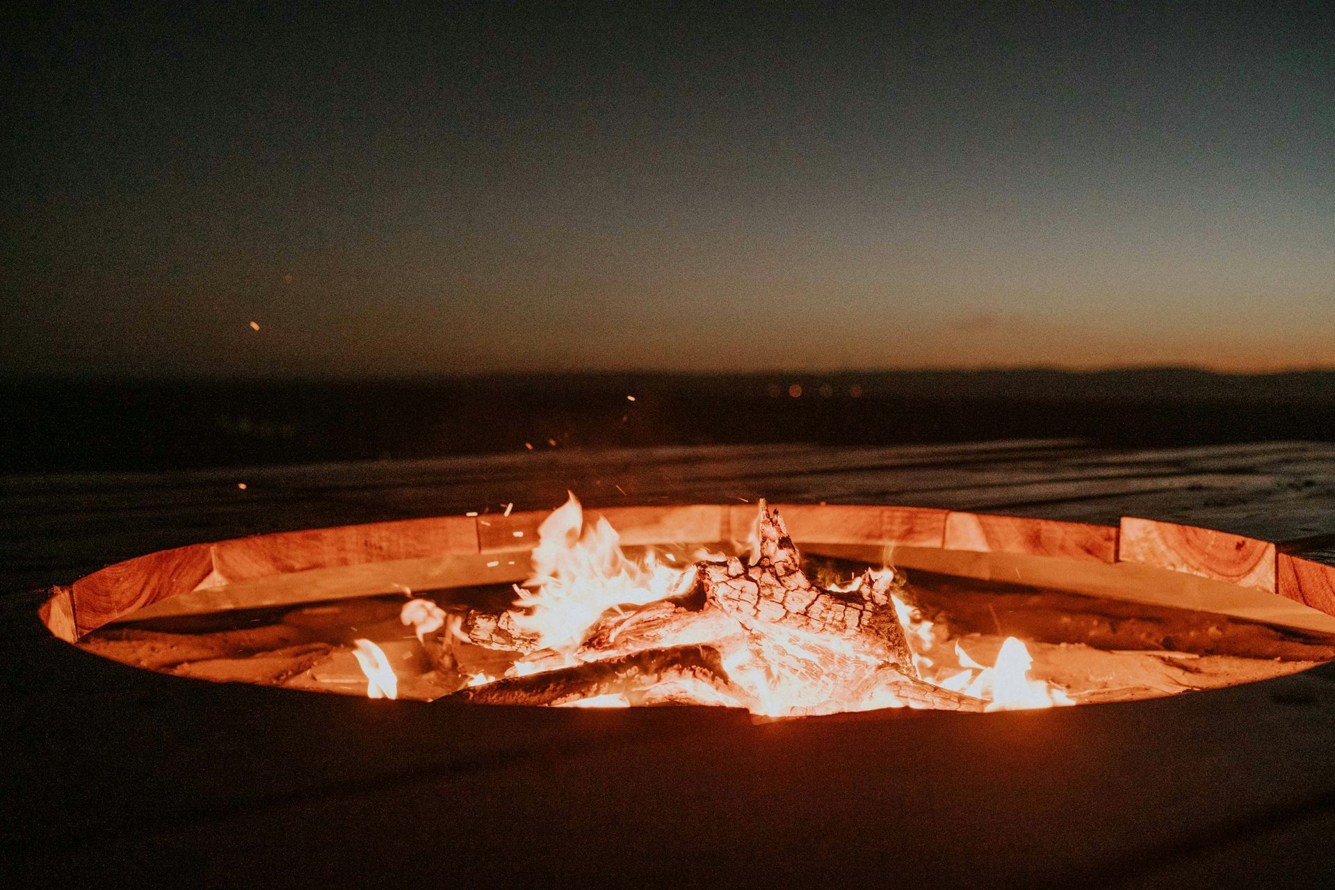 Fire burning in a circular fire pit at night under a dark sky