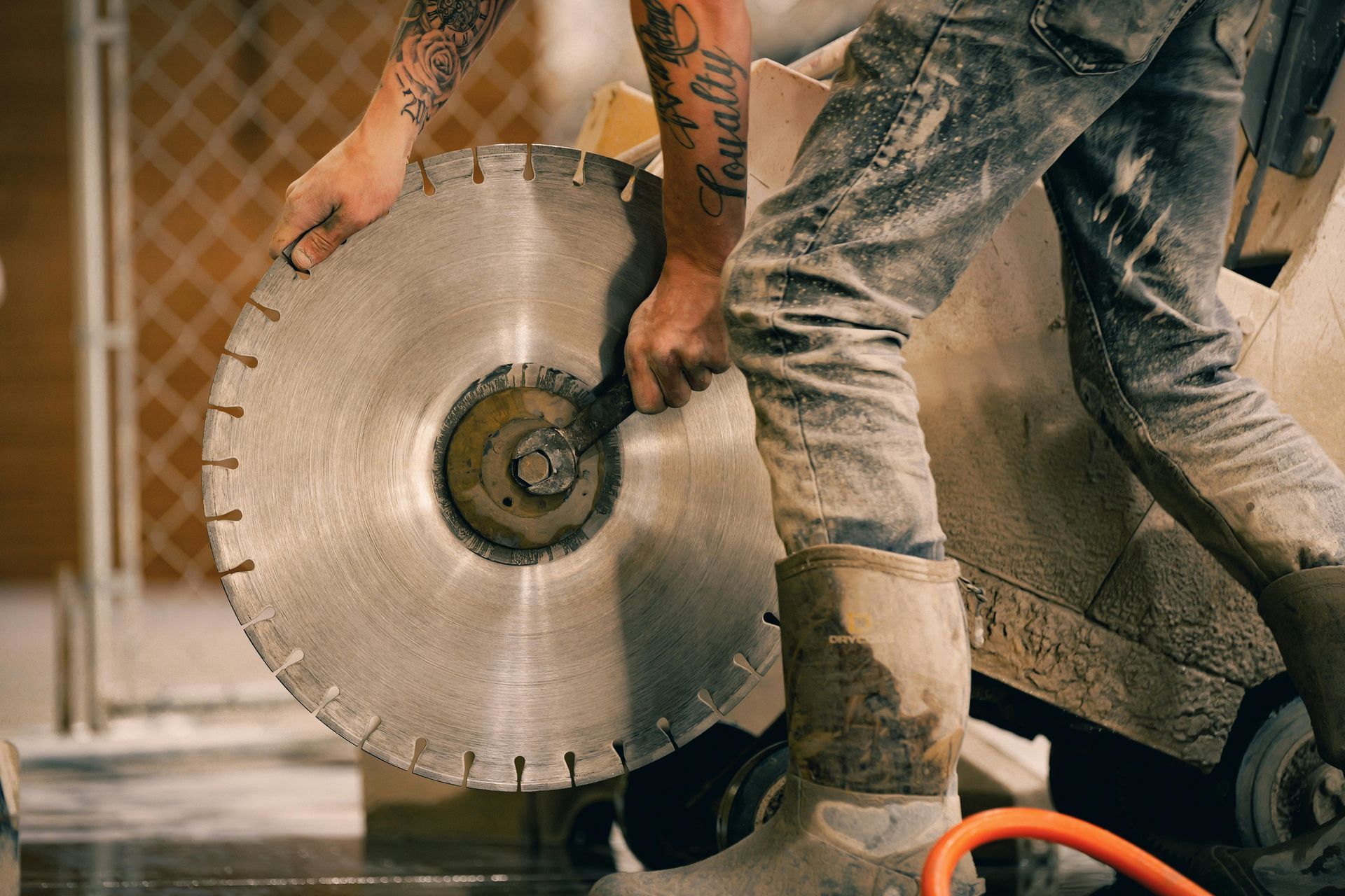 Worker handling a large circular saw blade at a construction site, with dust and equipment nearby