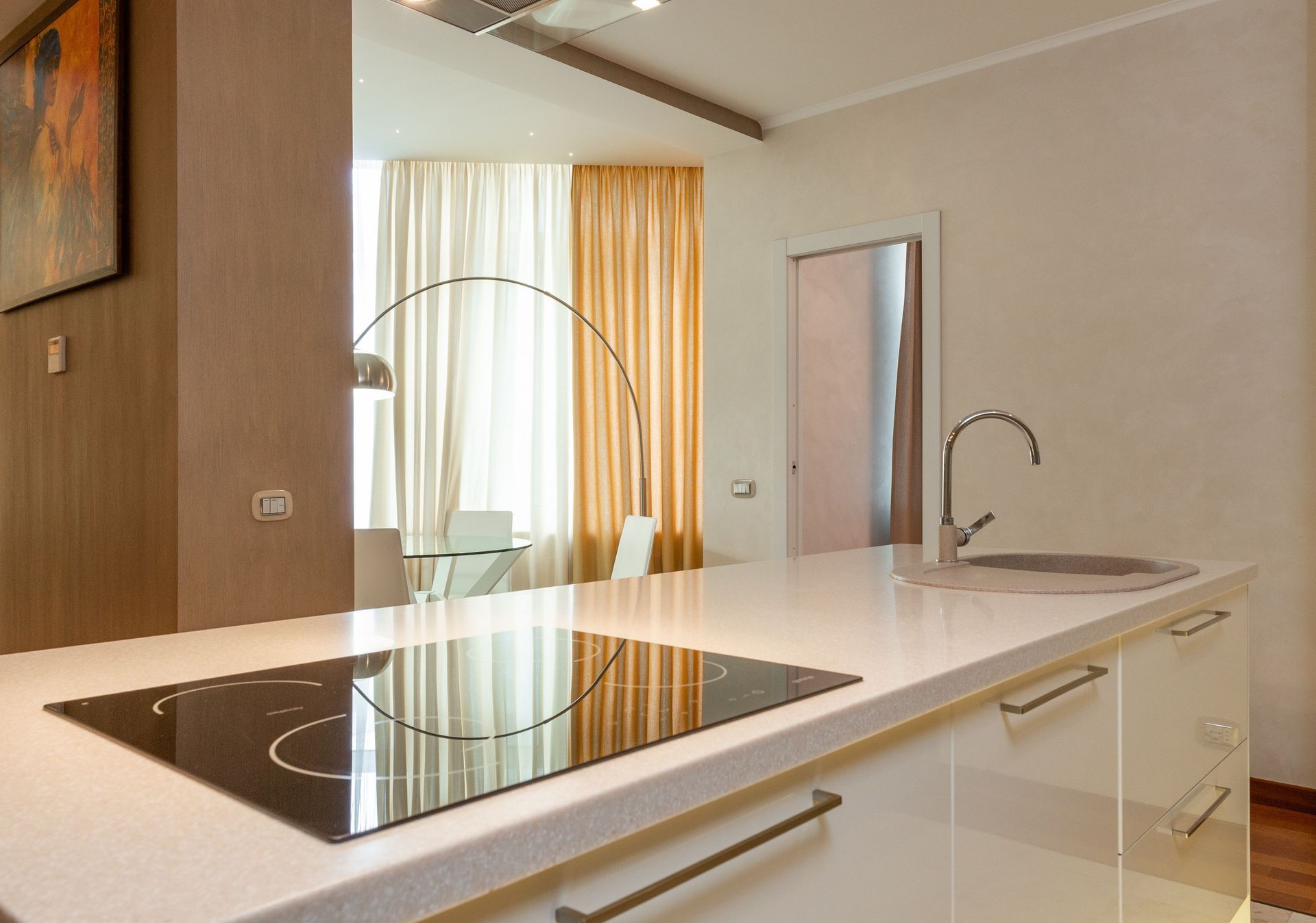 Modern kitchen with white island, black cooktop, sink, and window curtains