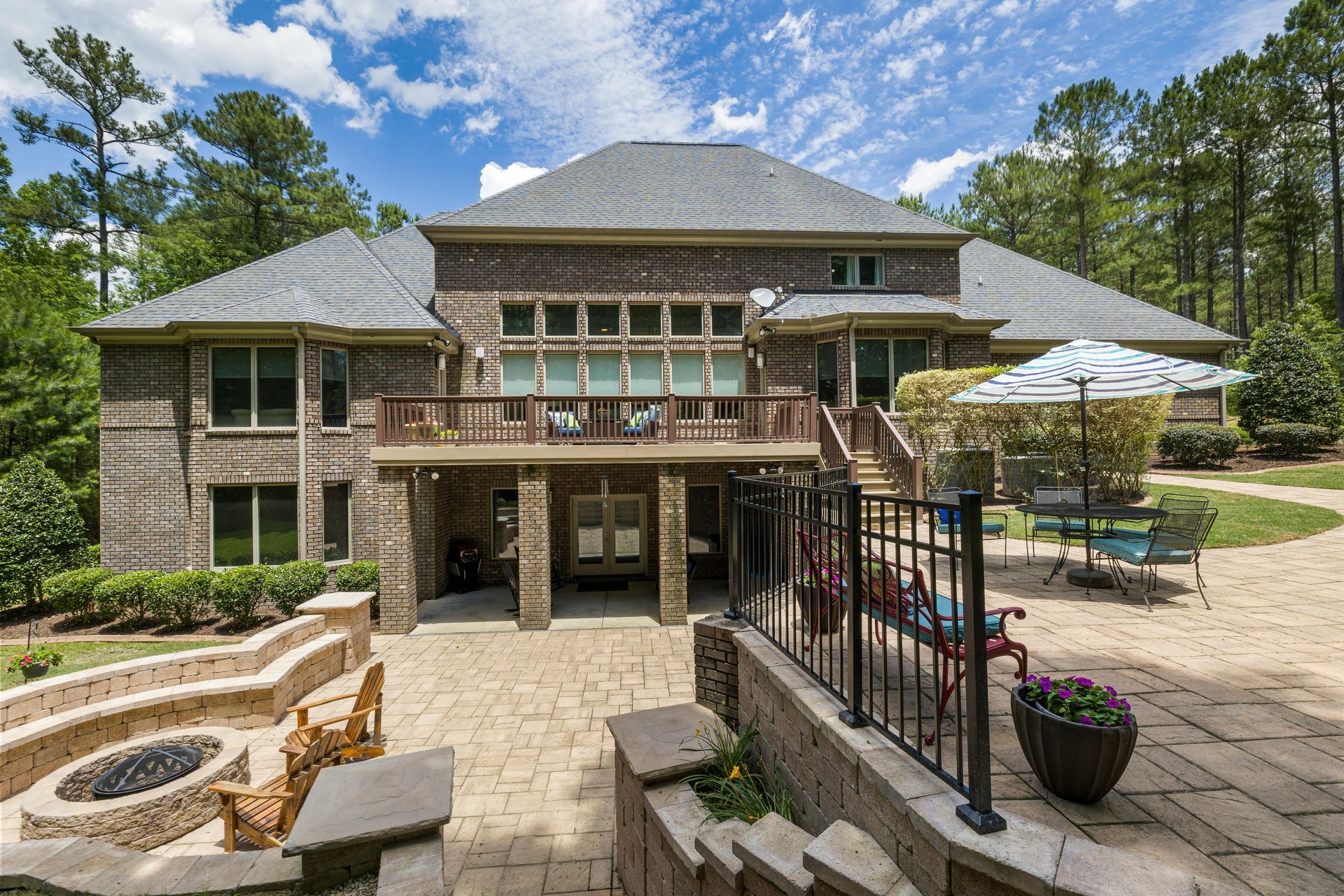 Spacious stone patio with outdoor seating, fire pits, and a two-story house under a blue sky
