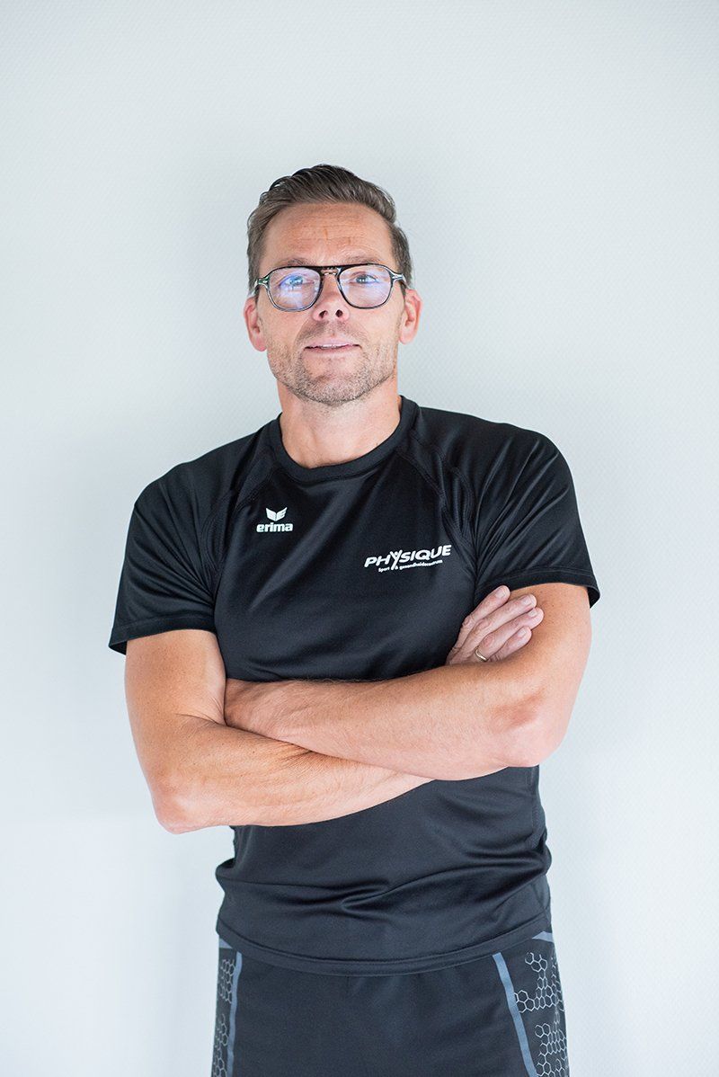 Een man met een bril en een zwart shirt staat met zijn armen over elkaar.