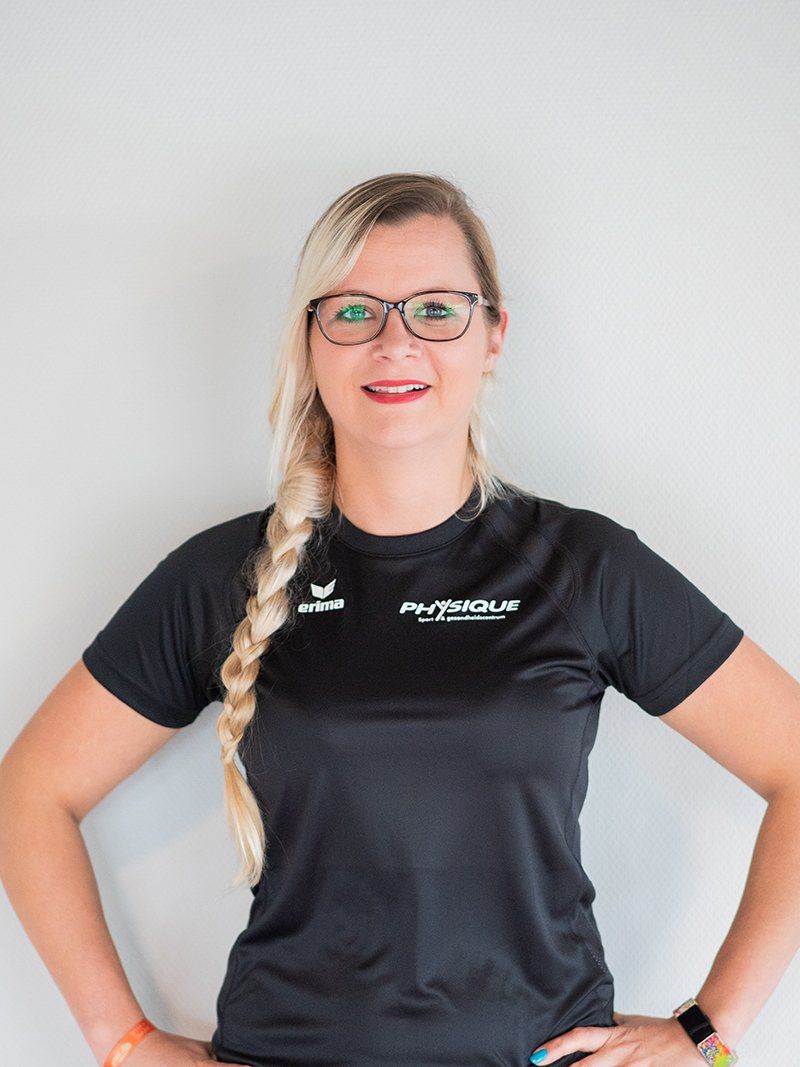 Een vrouw met een bril en een zwart shirt staat met haar handen op haar heupen.