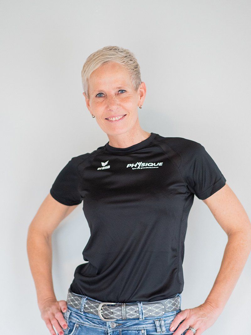 Een vrouw, gekleed in een zwart shirt en een spijkerbroek, staat met haar handen op haar heupen.