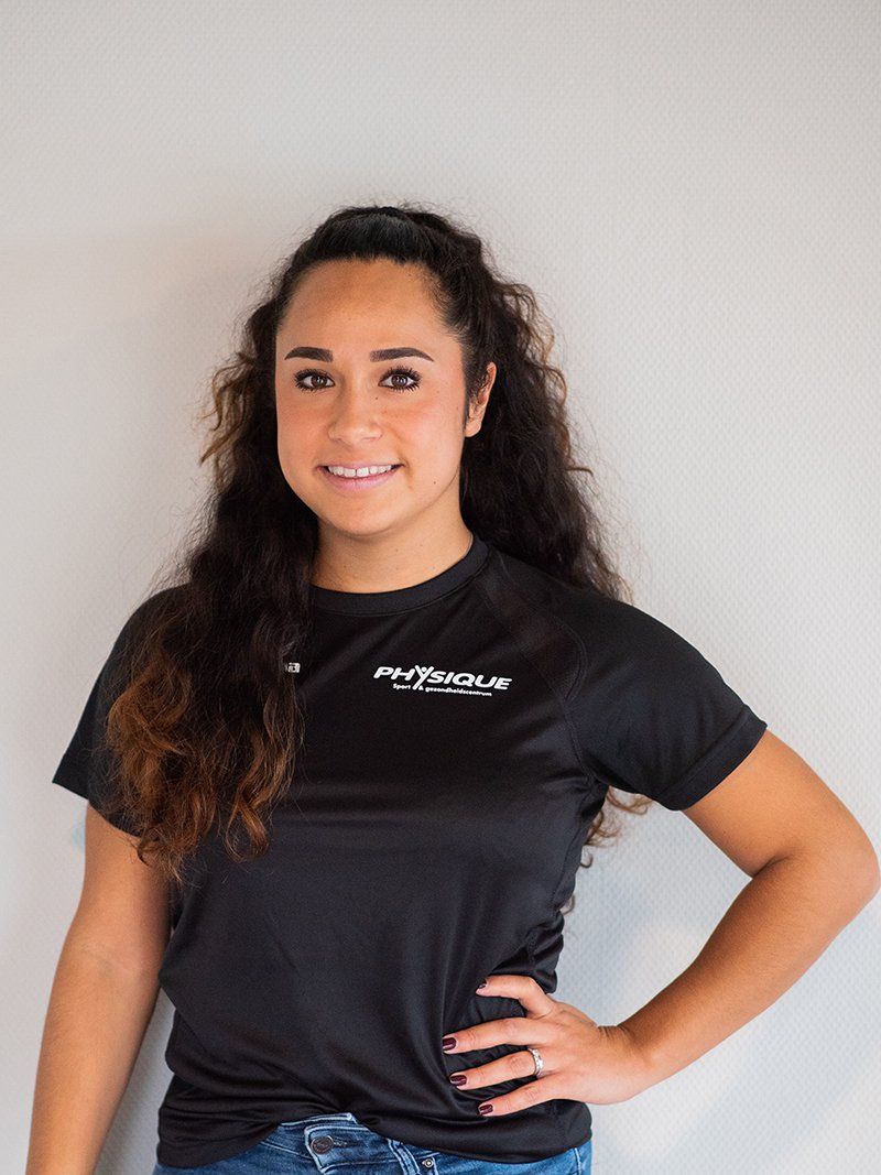 Een vrouw, gekleed in een zwart t-shirt, staat met haar handen op haar heupen.