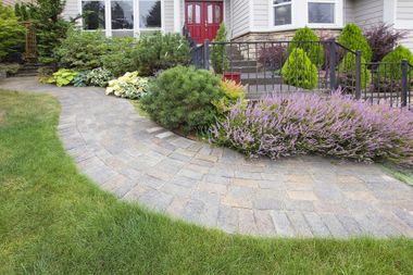 Aloha Concrete Pros custom paver walkway installation through a lush side yard with trees and flowers, showcasing our expertise in concrete pavers, paver patios, and paver driveway services.