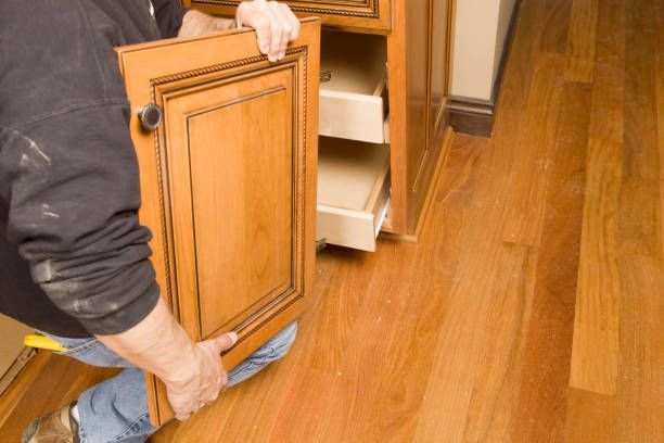 A man is kneeling down holding a wooden cabinet door.