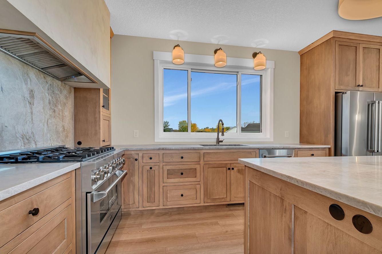 Modern kitchen with wood cabinets, stainless appliances, a large window, and a central island.