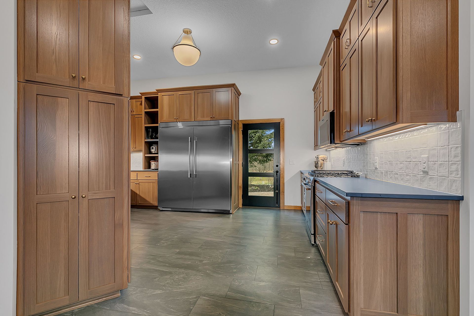 Kitchen with wood cabinets, stainless steel refrigerator, and gray concrete floor.