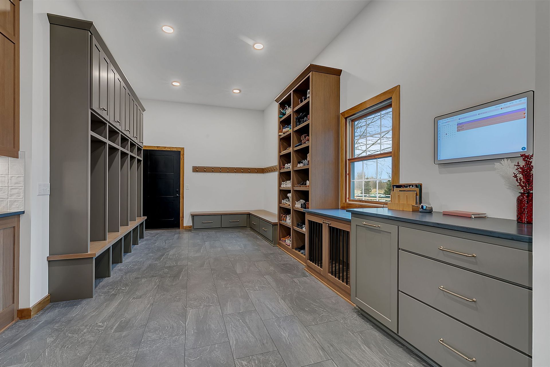 Mudroom with gray lockers, shoe shelves, bench, and cabinets. Gray flooring and white walls.