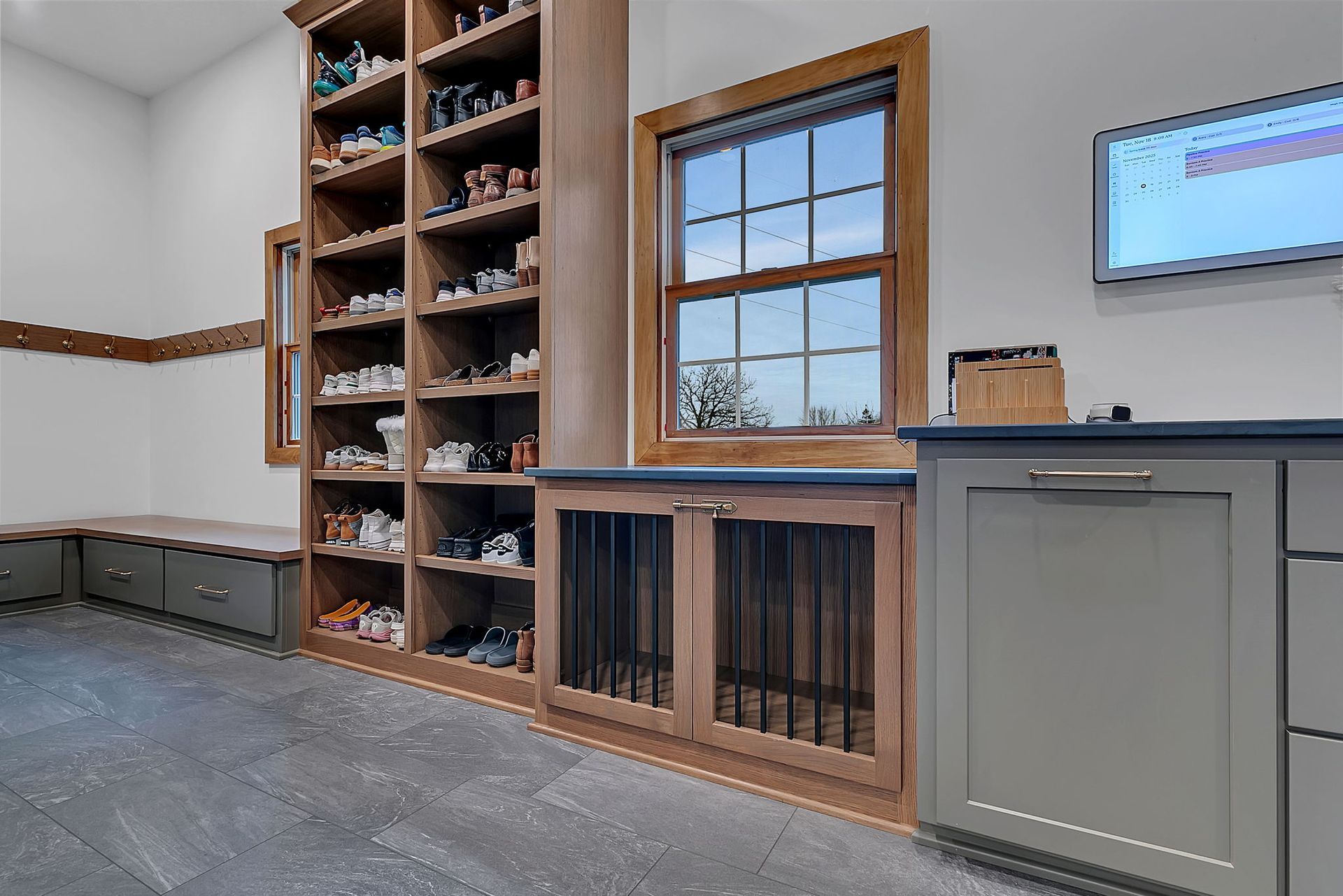 Built-in storage area with shoe shelves, dog crate, window, and cabinetry; dark gray flooring.