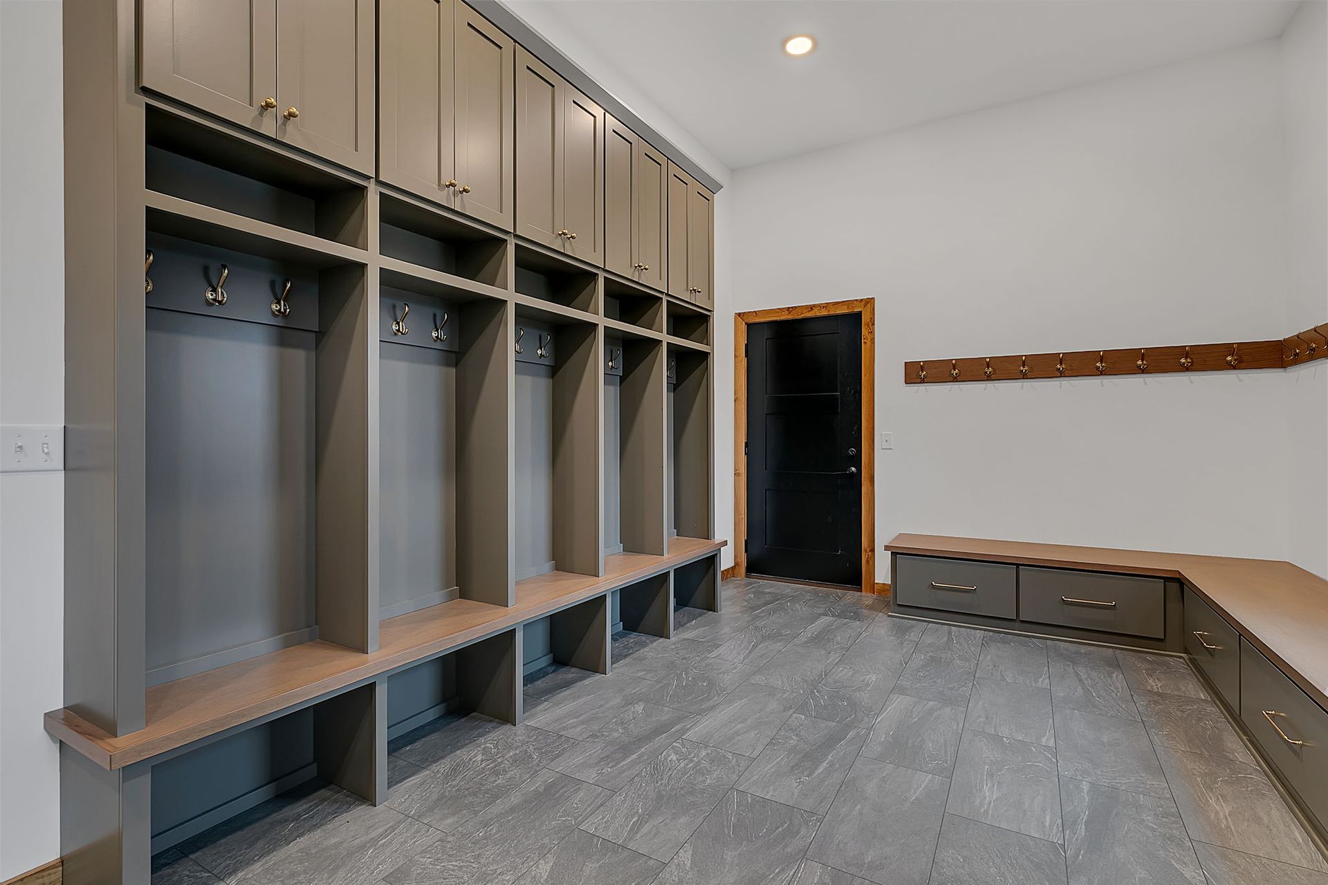 A grey mudroom with lockers, bench, hooks, and a black door.