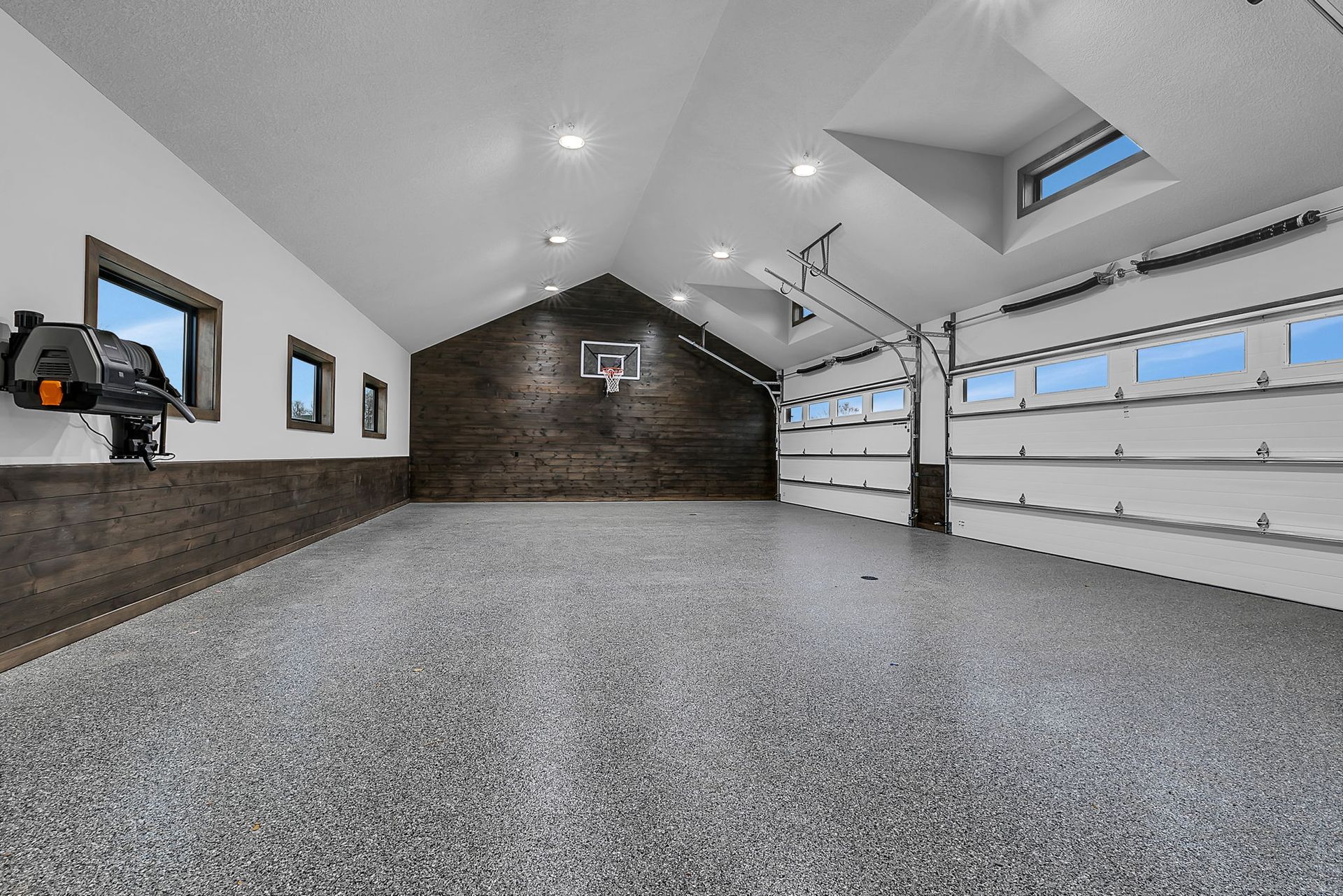 Spacious garage with basketball hoop, epoxy floor, skylight, and open garage door.
