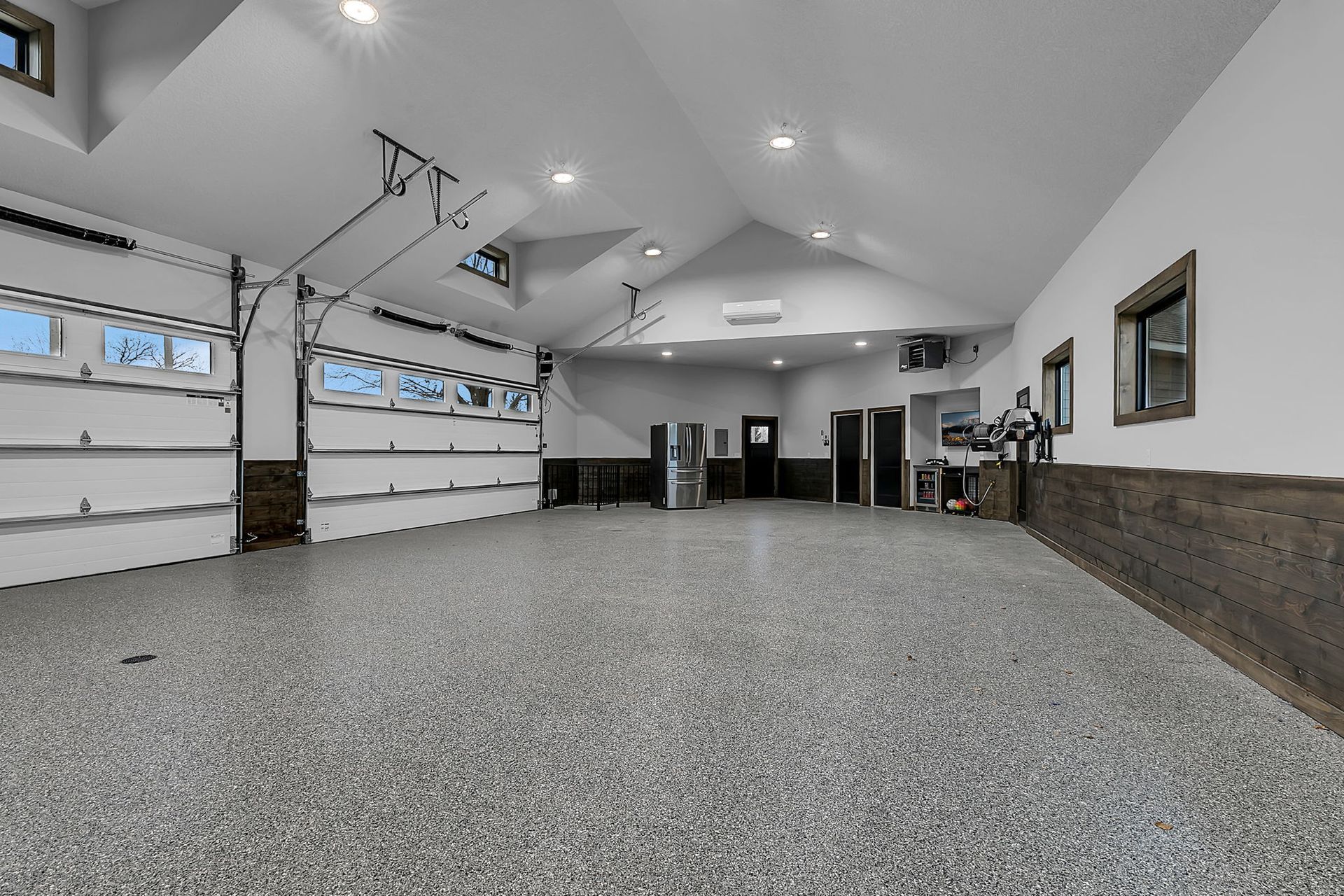 Spacious garage with epoxy floor, three overhead doors, and wood paneling on the walls.