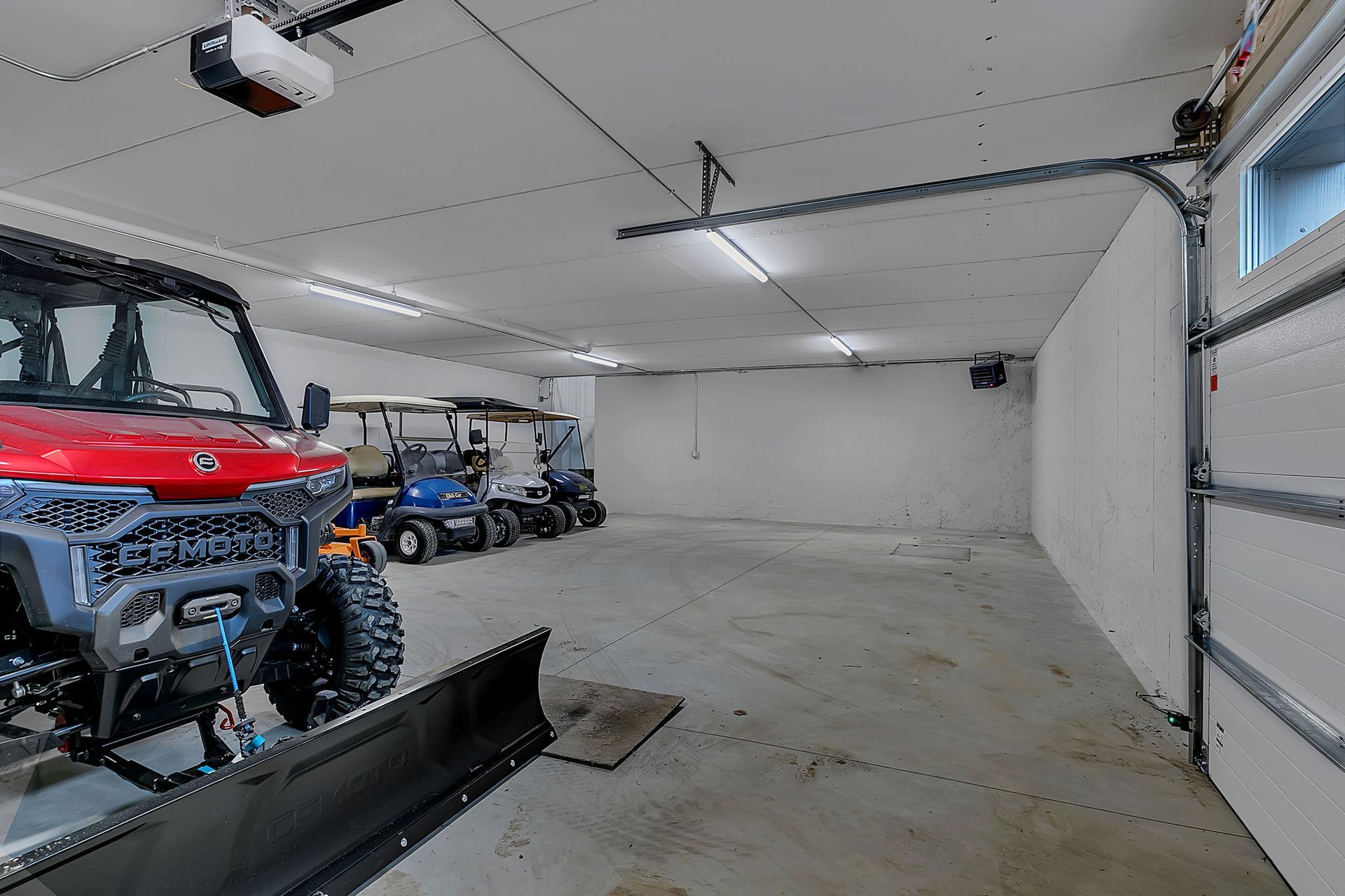 Garage with red UTV and golf carts, concrete floor, white walls and ceiling.