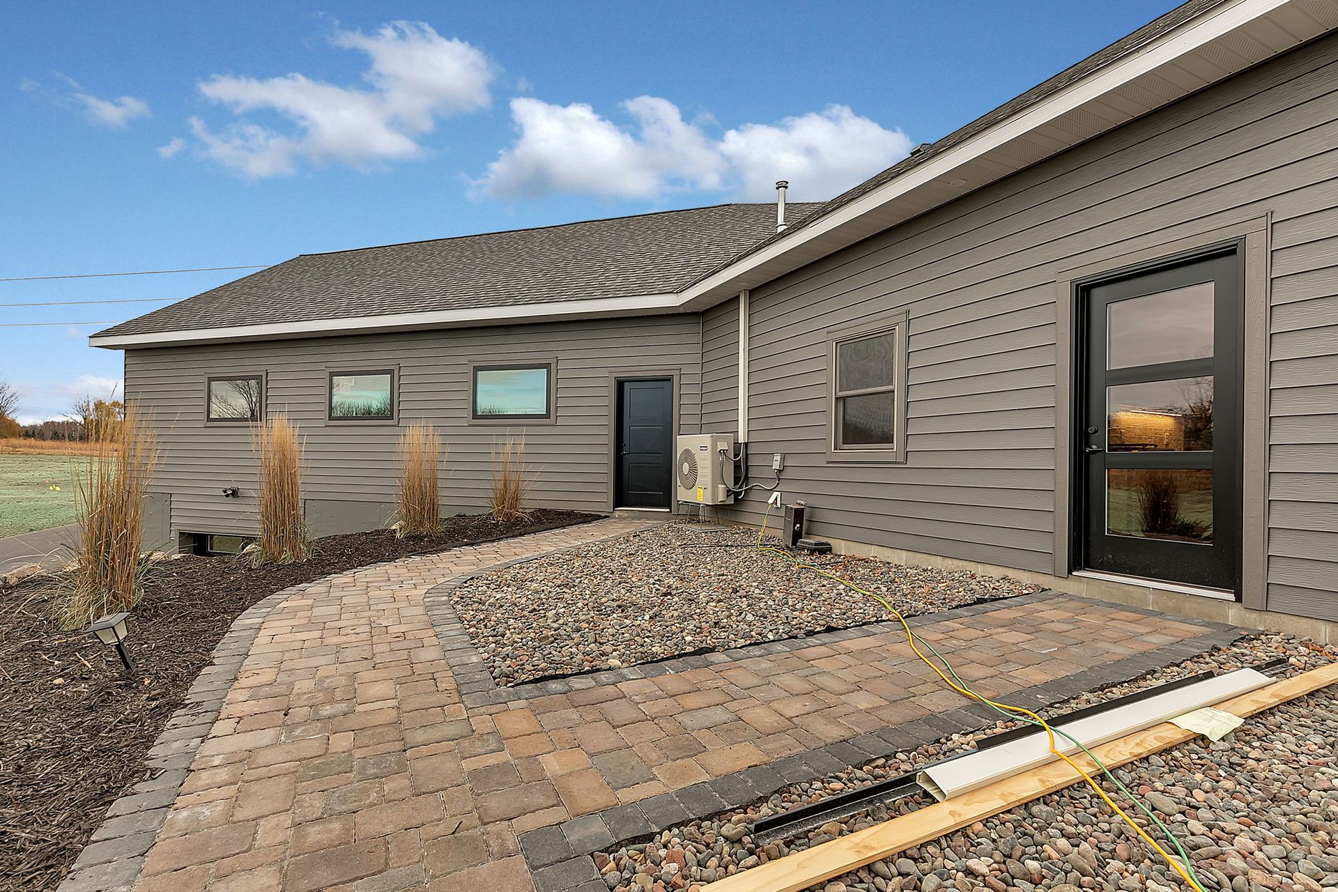 Exterior of a modern house with gray siding, dark door, and paved patio area.