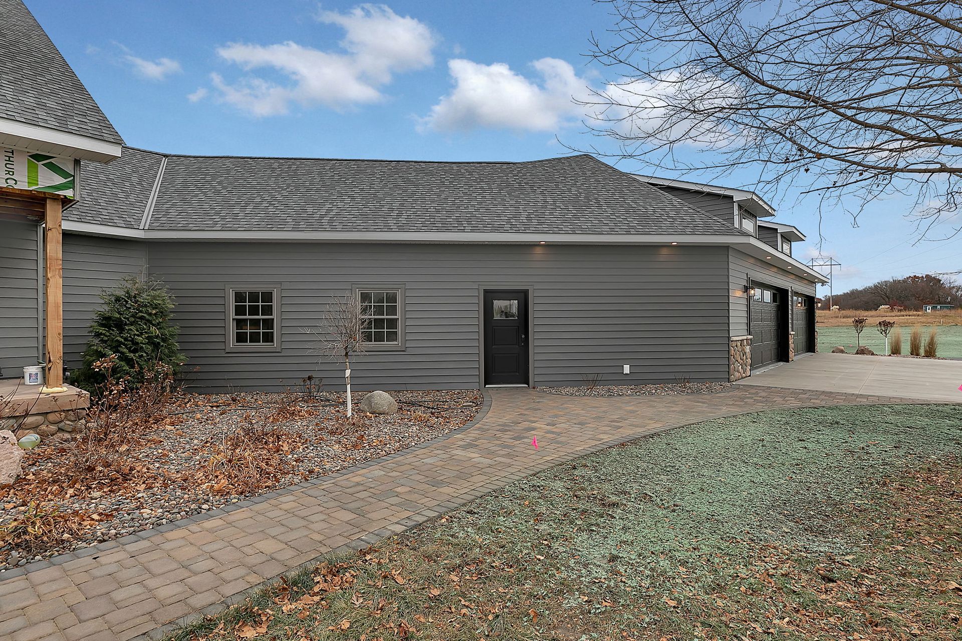 Gray house with a brick walkway and a driveway; blue sky with clouds in the background.
