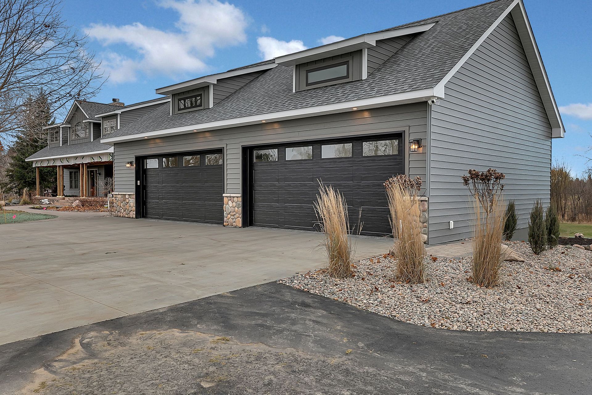 Two-car gray garage with black doors and matching gray siding, set on a gravel driveway under a blue sky.
