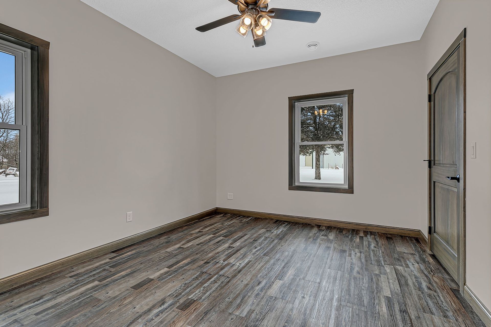 Empty bedroom with gray walls, dark wood floor, windows, and ceiling fan.