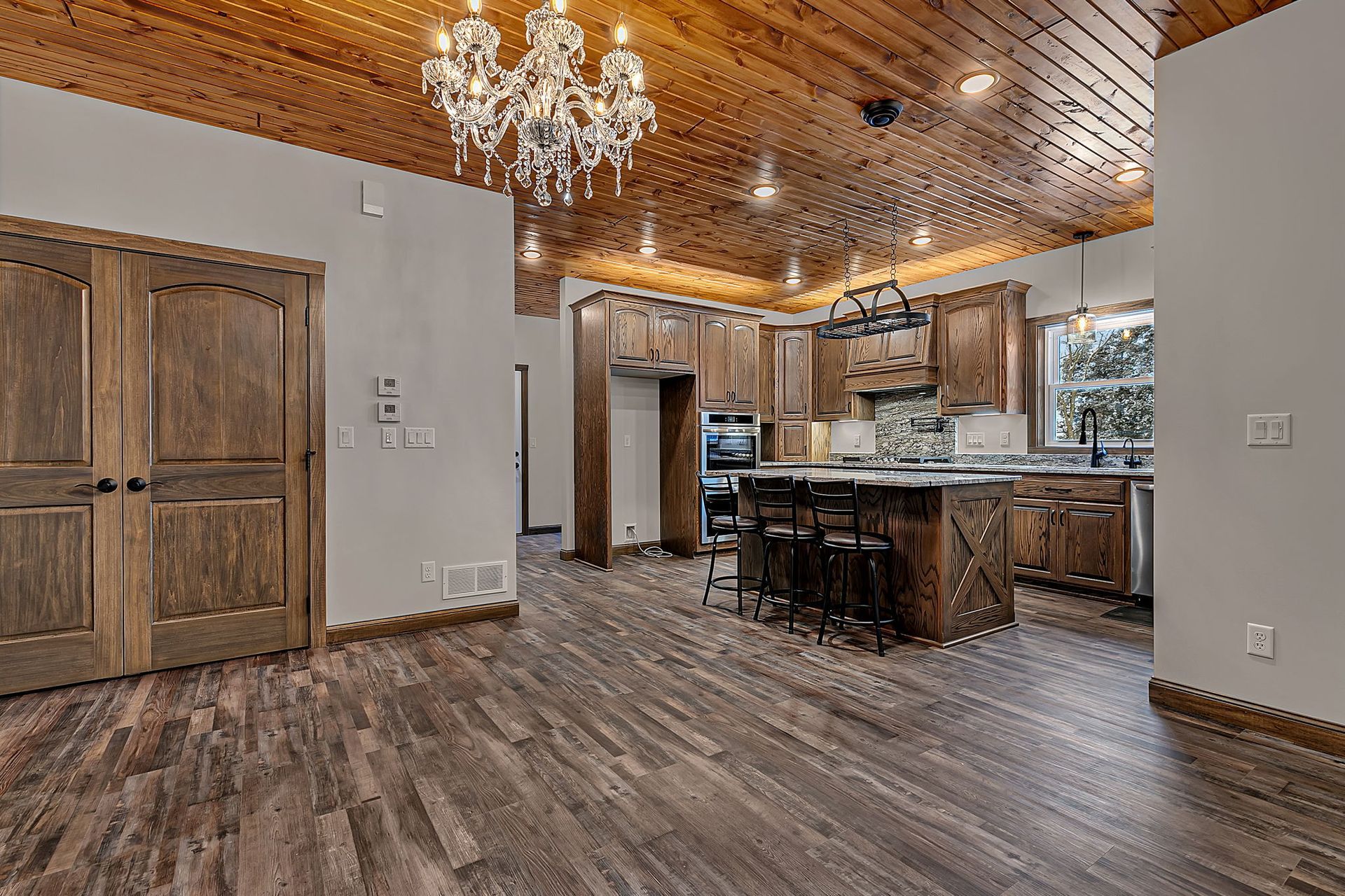 Kitchen with wood ceiling, cabinets, and flooring; an island with stools, and a chandelier.