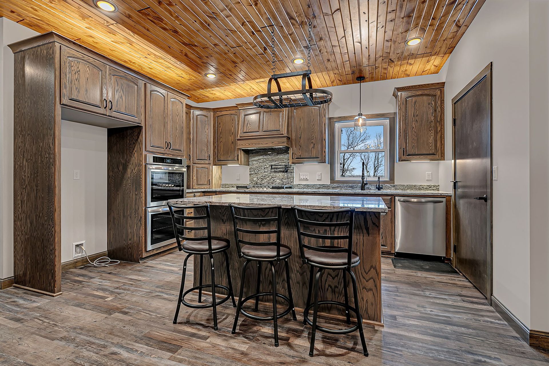 Rustic kitchen with wood cabinets, island, and ceiling, stainless steel appliances, and bar stools.