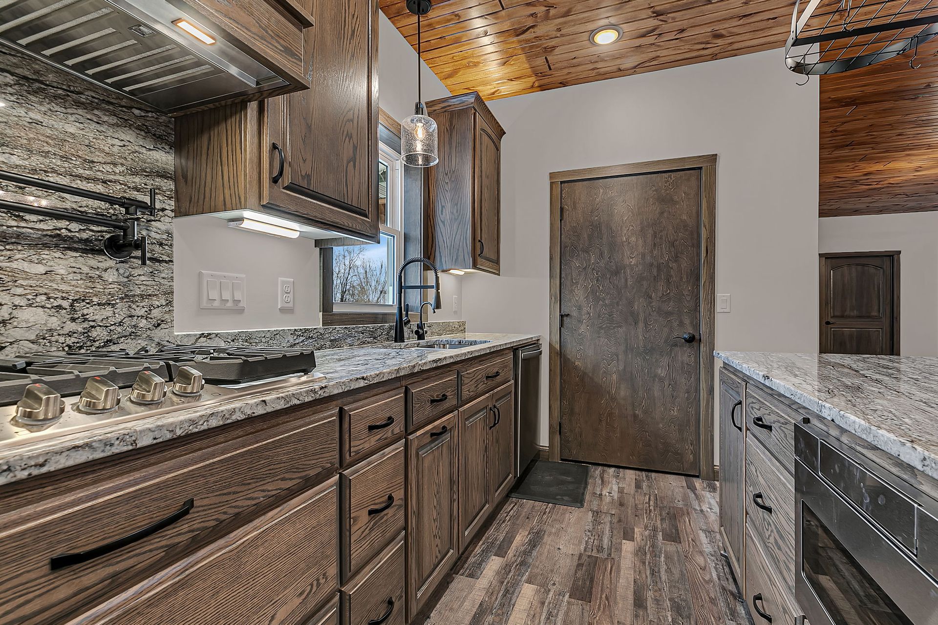 Rustic kitchen with wood cabinets, granite countertops, and patterned ceiling.
