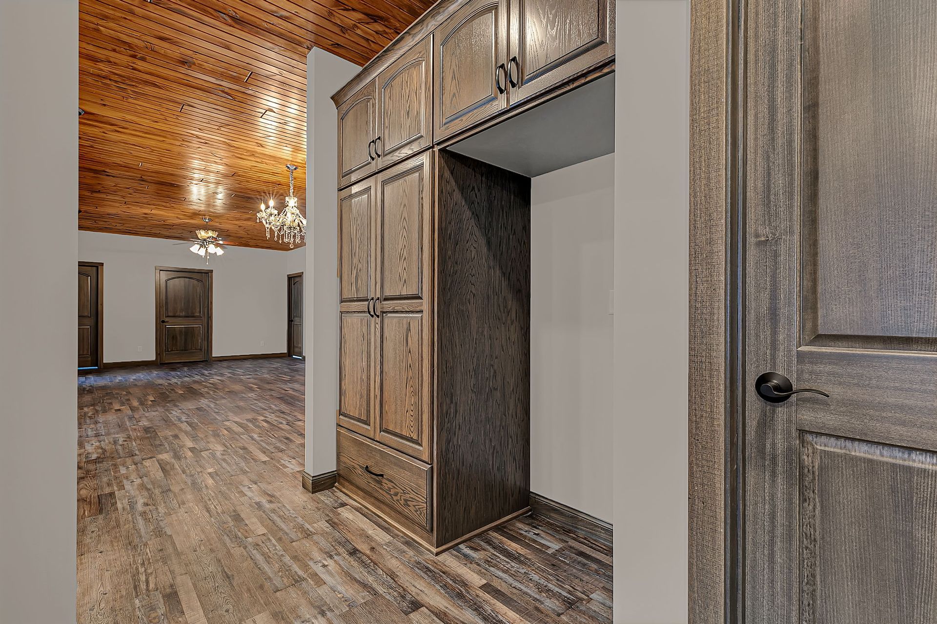 Wooden cabinets frame a refrigerator space in a room with wood floors and a decorative ceiling.