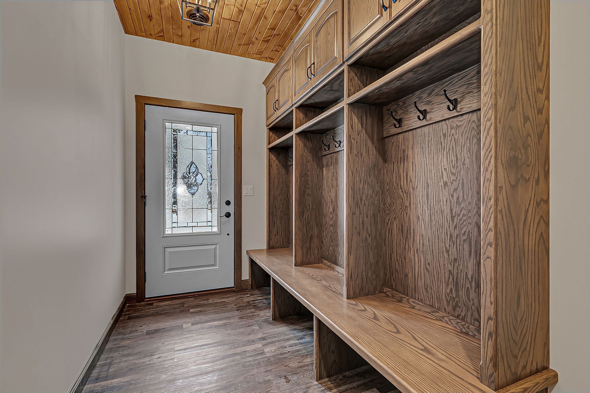 Entryway with wooden lockers and bench, front door on left, wood ceiling.