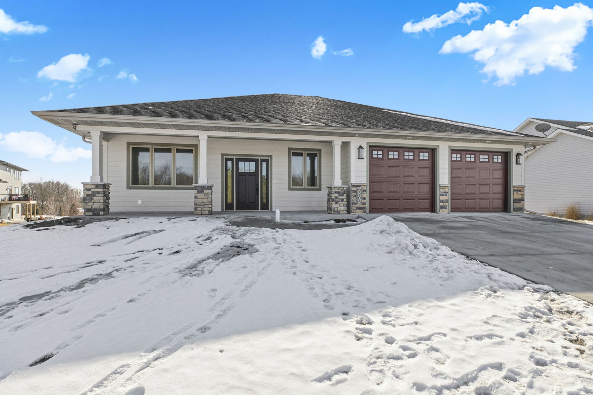 Gray house with brown garage doors and snow in front under a blue sky.