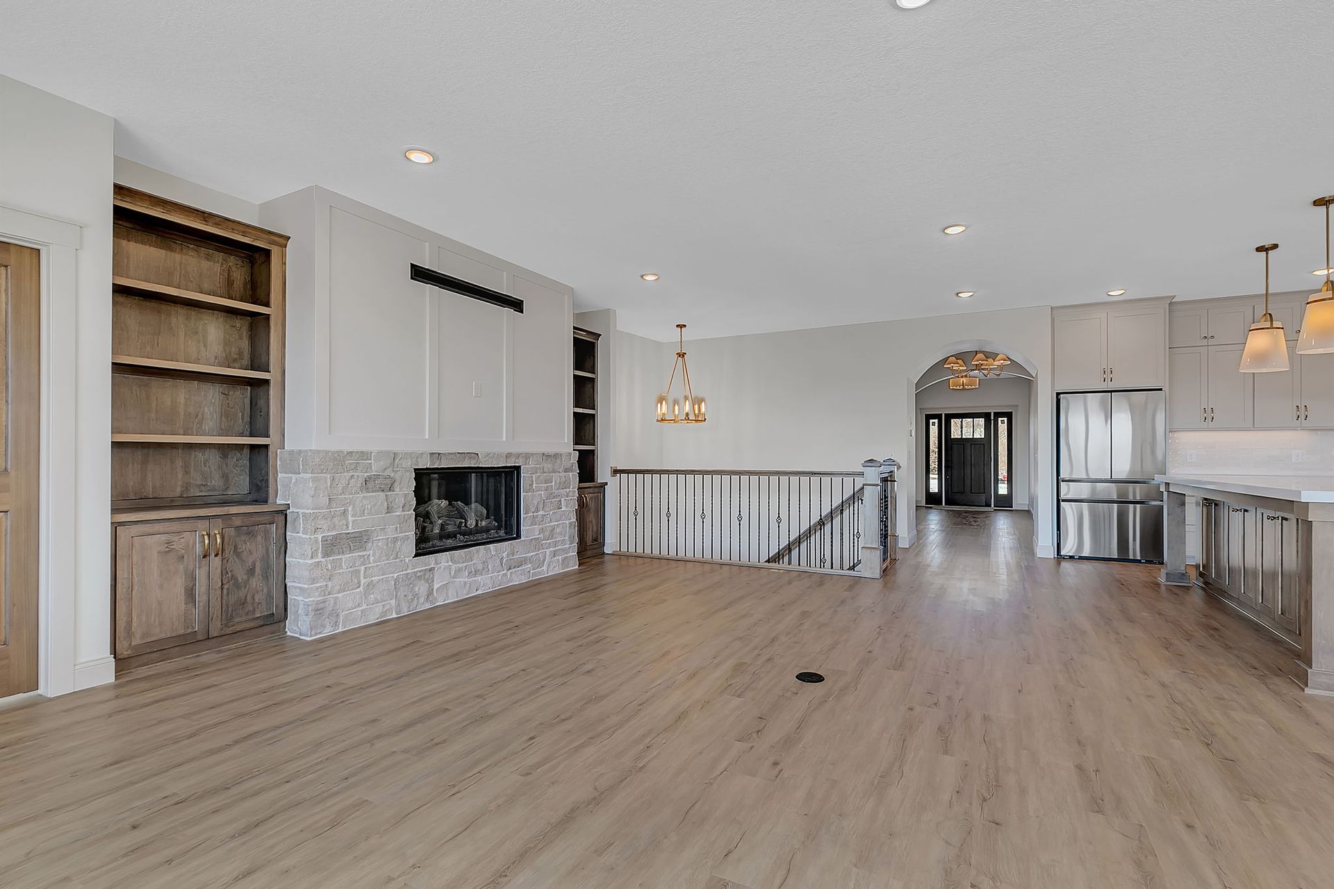 Spacious, modern living room with fireplace, built-in shelves, and open kitchen. Pale wood floors and white walls.