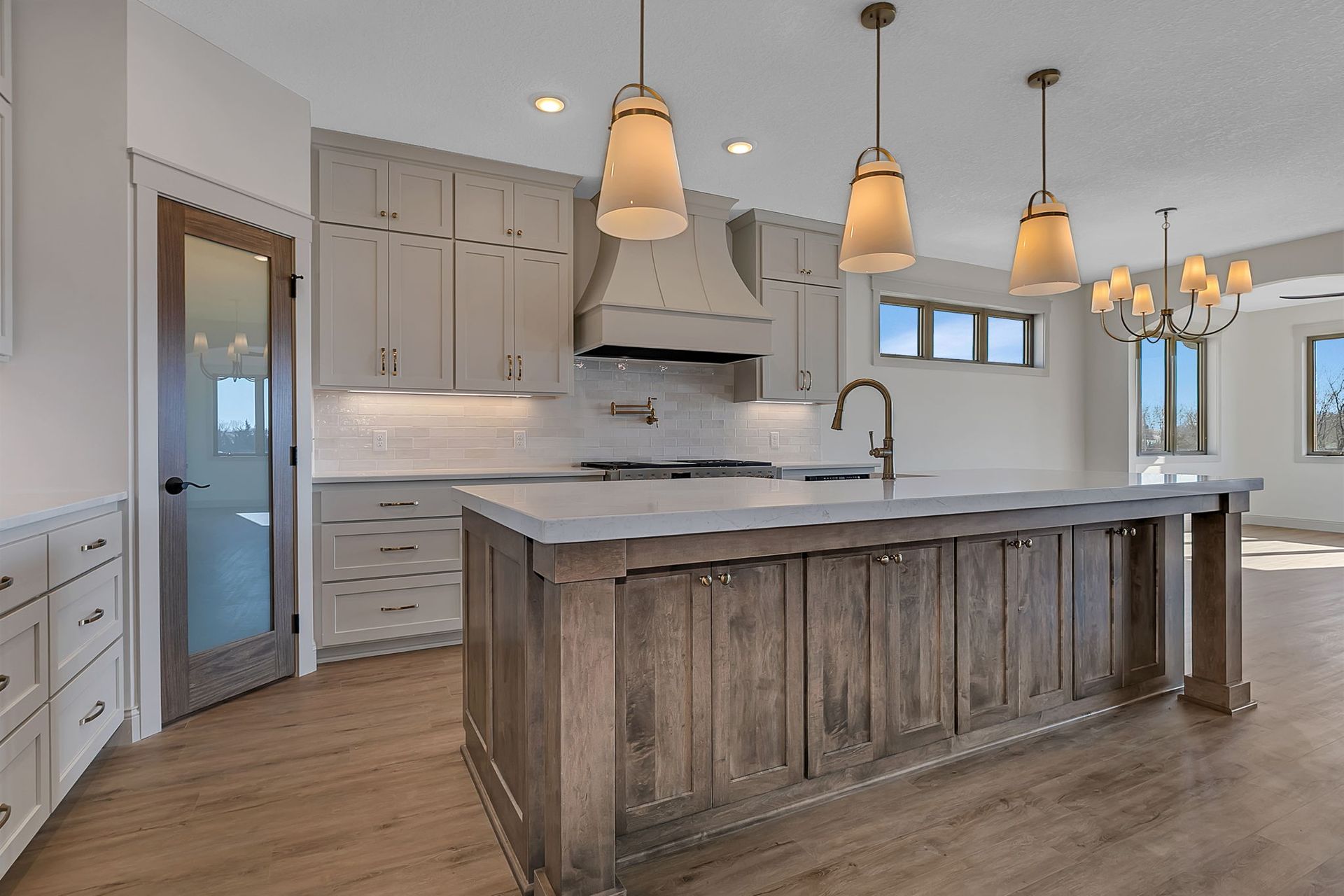 Modern kitchen with a gray island, light cabinets, and pendant lights.