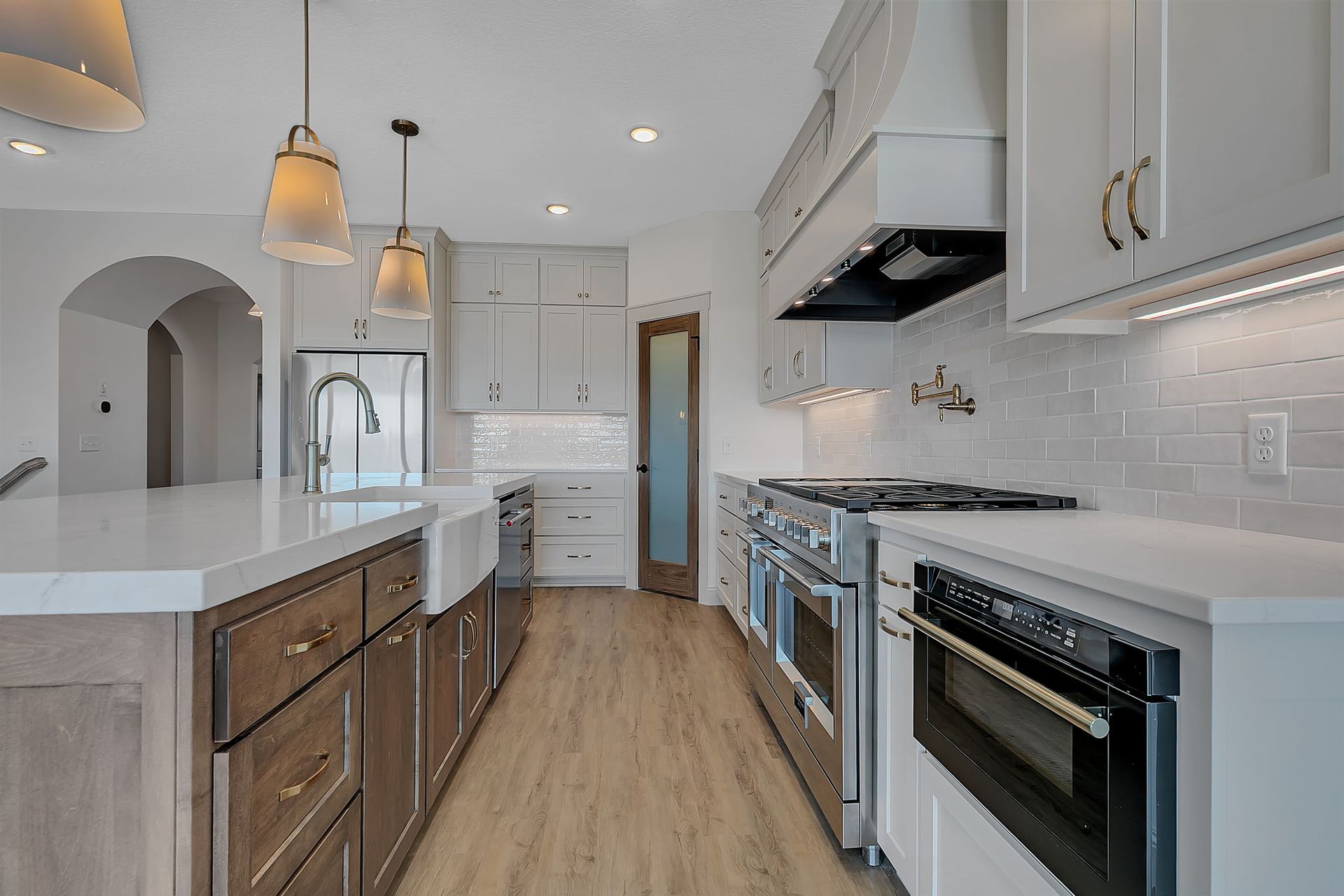 Spacious kitchen with a large island, stainless steel appliances, white cabinets, and wood flooring.