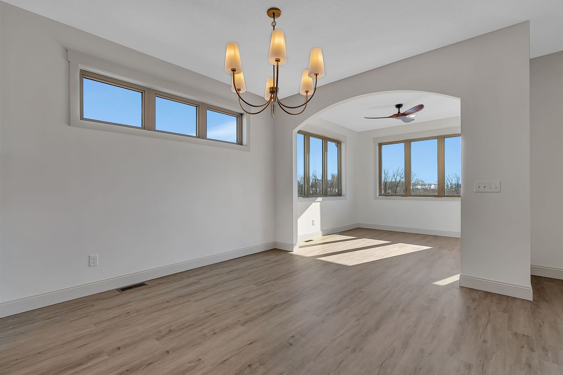 Empty, bright dining room with wood floors, arched doorway, and chandelier.