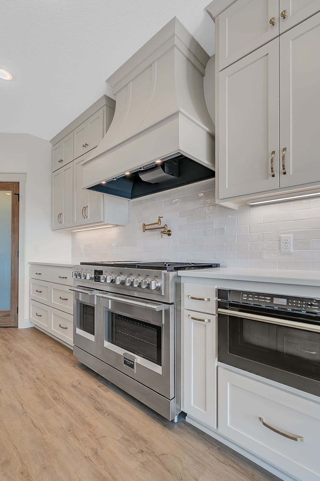 Kitchen with stainless steel range, white cabinets, light gray range hood, and tile backsplash.