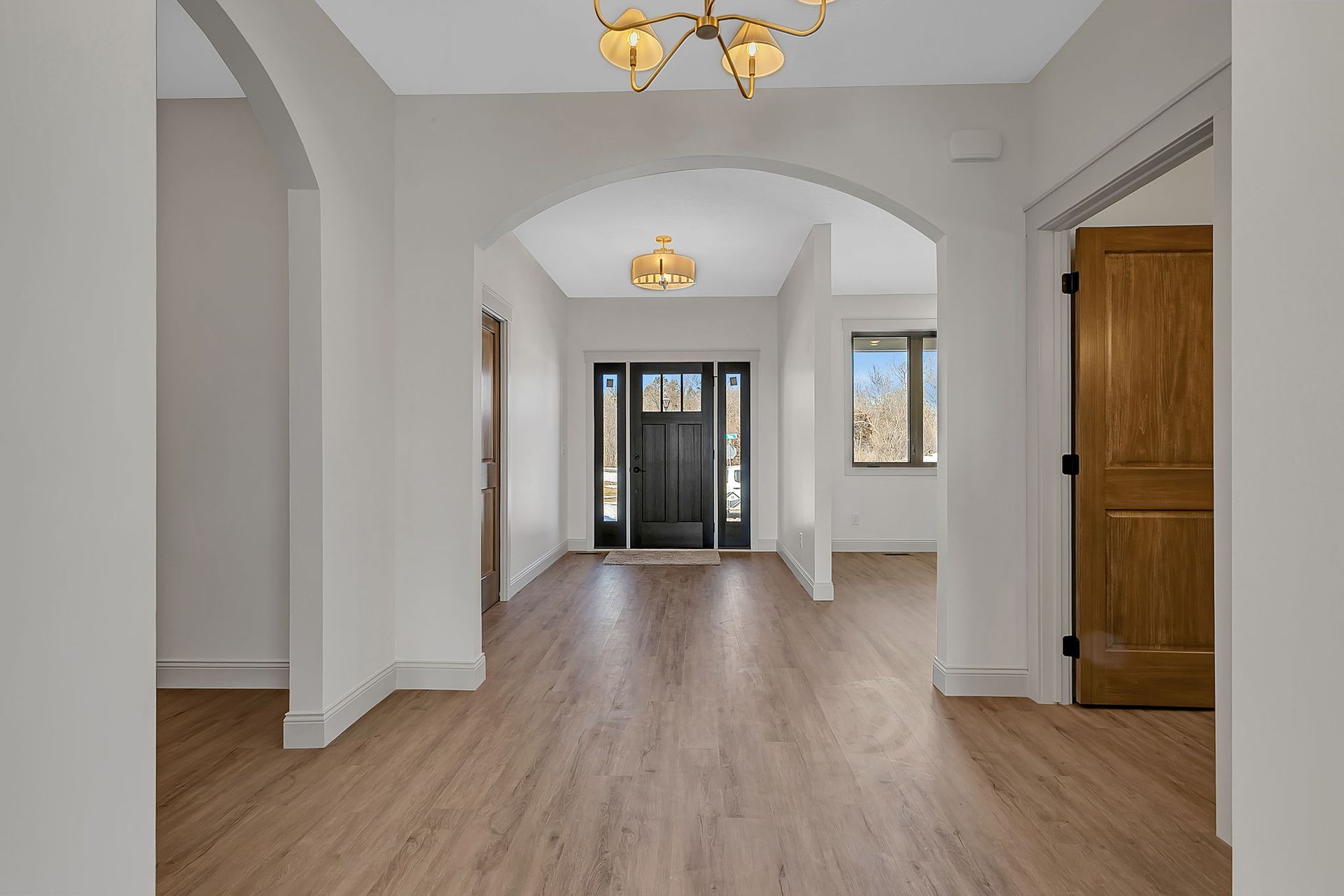 Hallway with light wood floors, white walls, arched doorways, and a black front door.