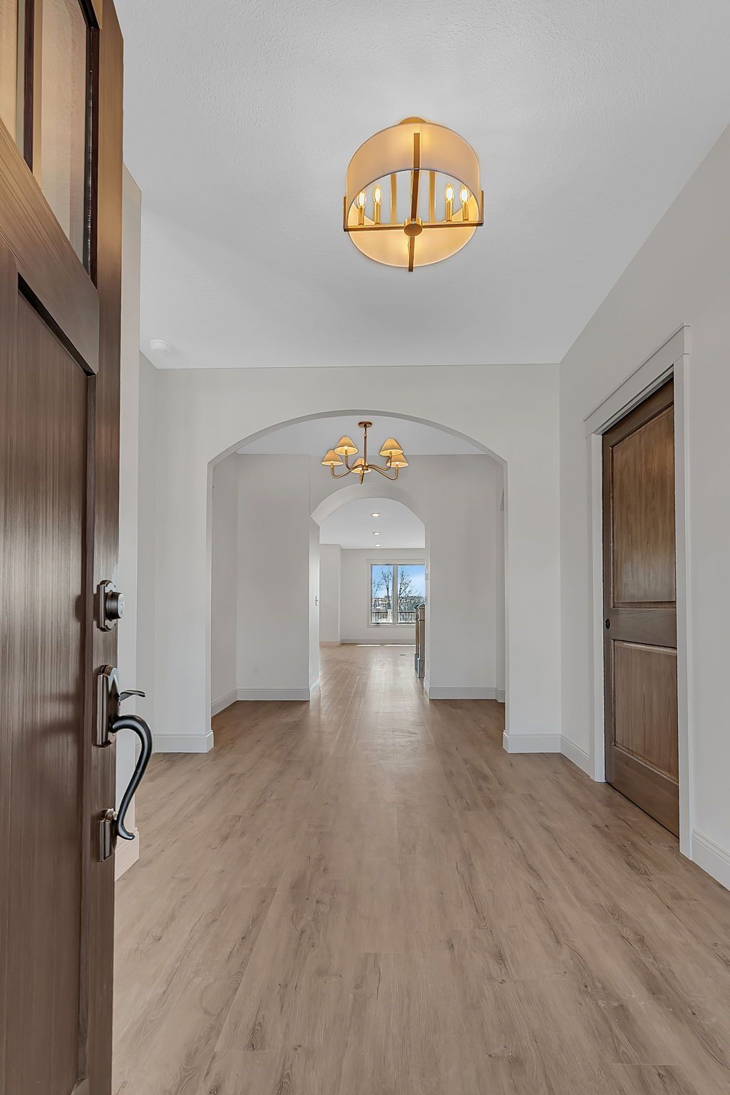 Entryway with light wood floors, white walls, and a view through arched doorways to another room.