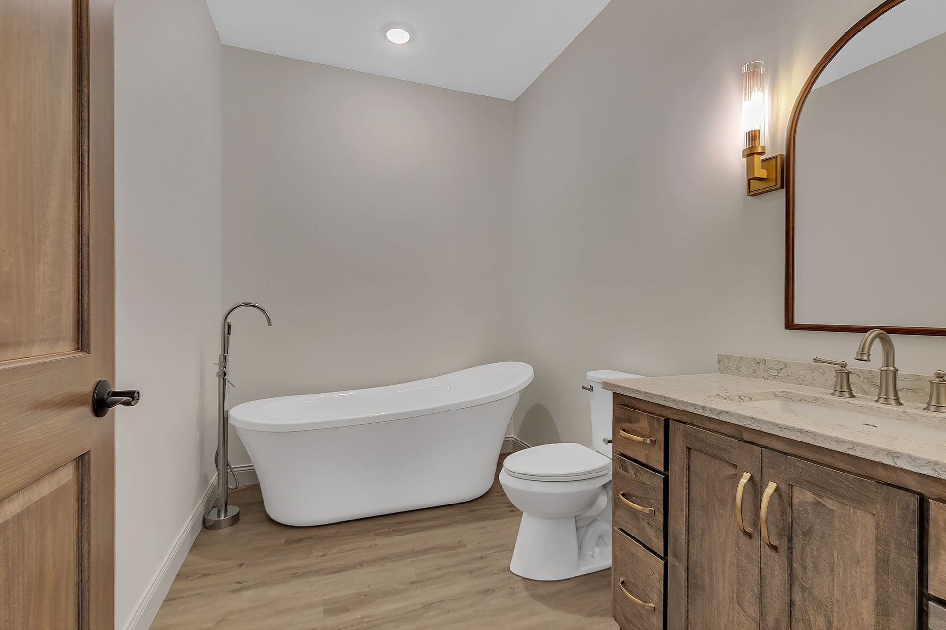 Bathroom with a white freestanding tub, wood vanity, and a toilet.