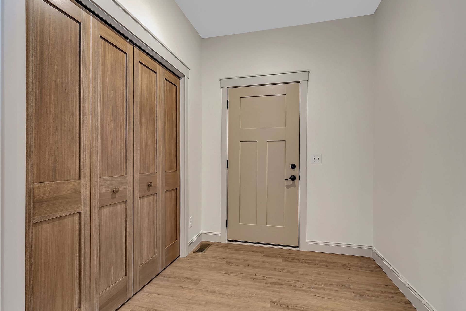 Hallway with light brown door, closet with wooden doors, and beige walls.