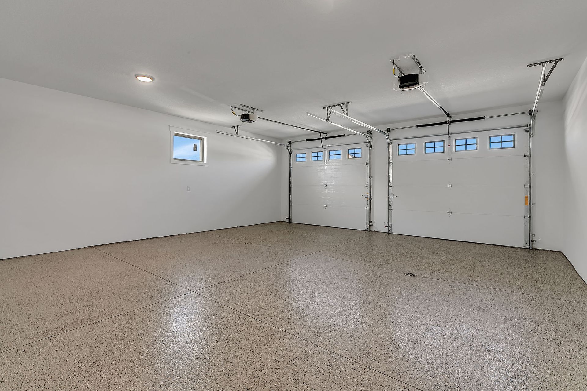 Empty, well-lit garage with two closed doors, concrete floor, and small window.