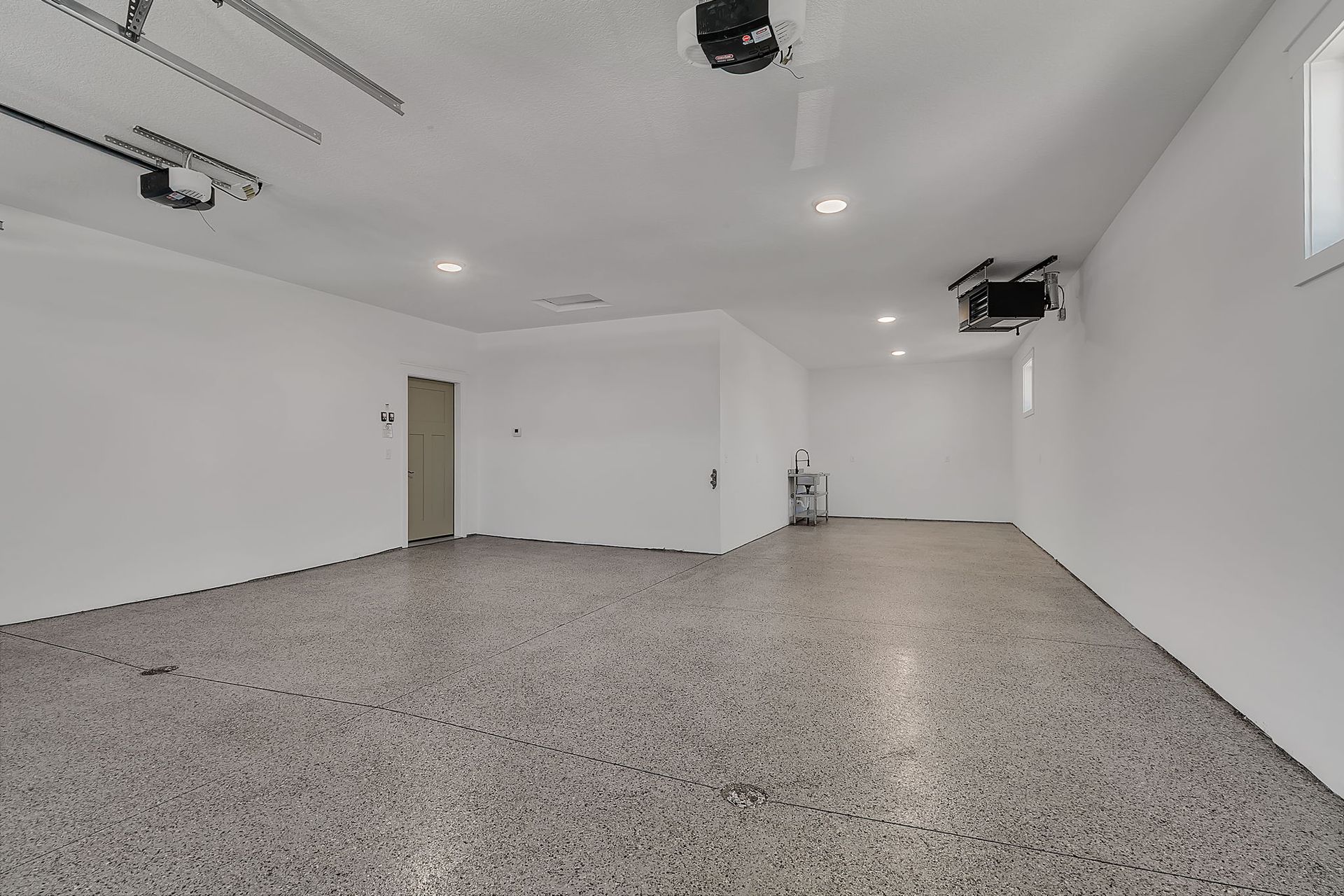 Empty garage with a speckled gray floor and white walls. Garage door opener on the ceiling.