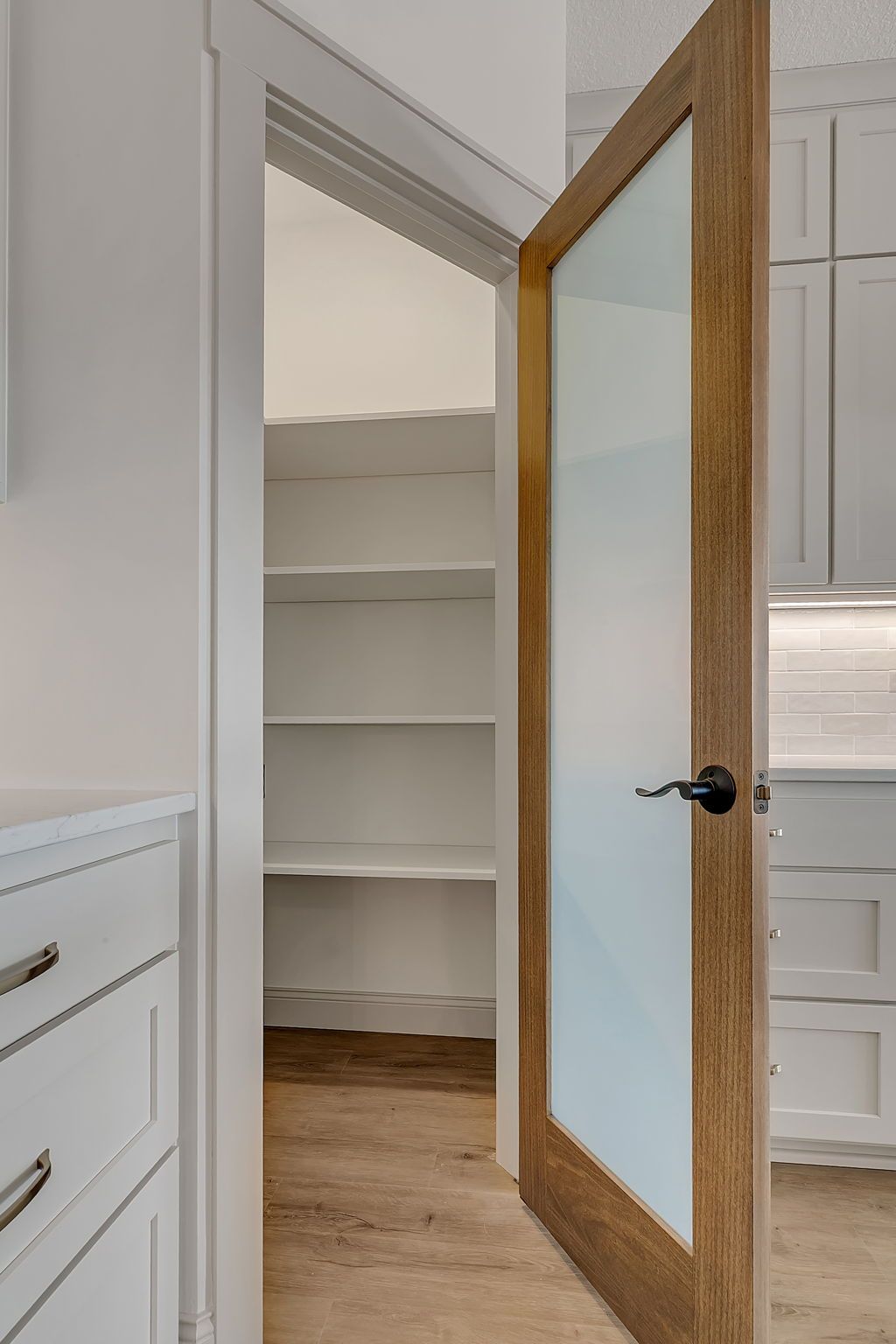 Open pantry with shelves, wooden door, frosted glass, white cabinets.