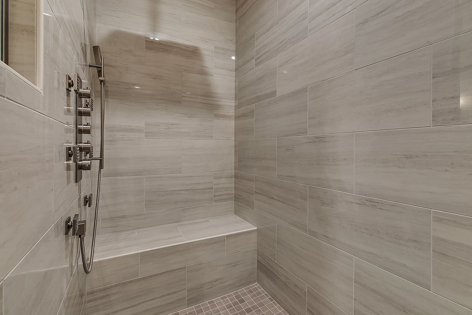 A tiled shower with a built-in bench and multiple showerheads. Gray walls and a silver fixture.