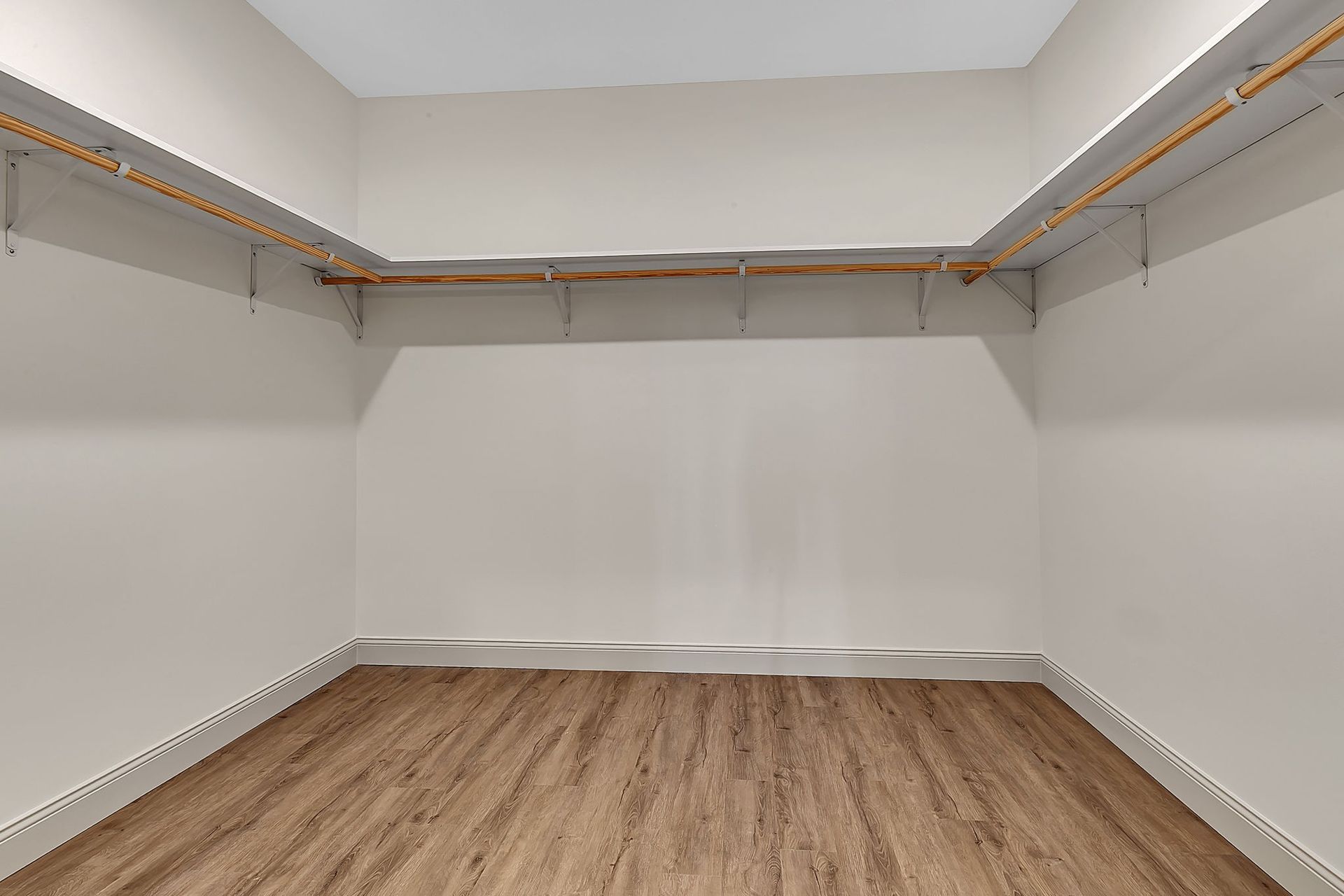 Empty walk-in closet with wooden shelves and flooring; beige walls.